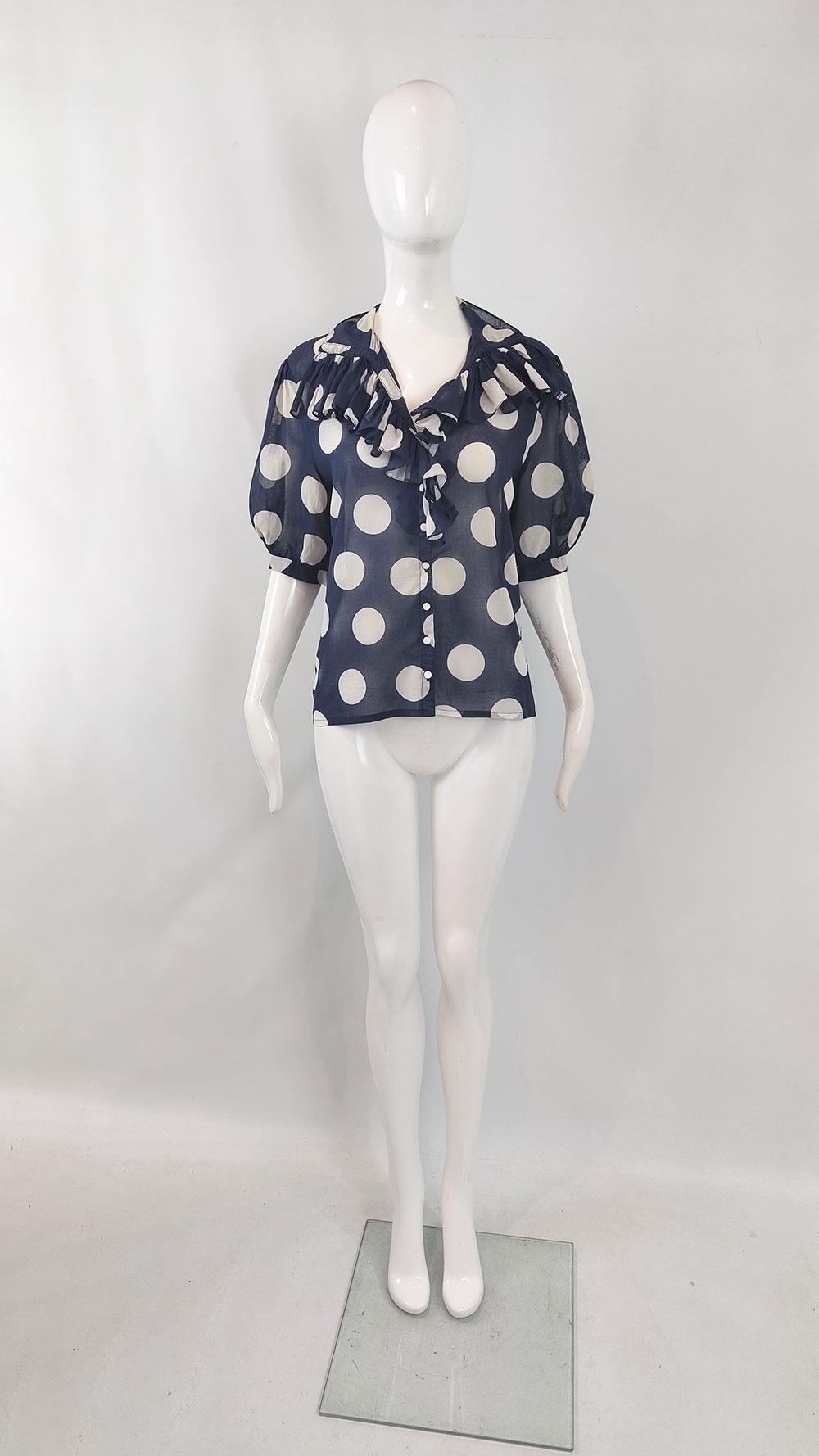 A charming 80s vintage blouse by designer Jean Dessés. Made from sheer navy cotton voile with oversized cream polka dots, it boasts puff sleeves and a frilly collar for a playful look. Jean Dessés, a celebrated designer, was linked with Valentino