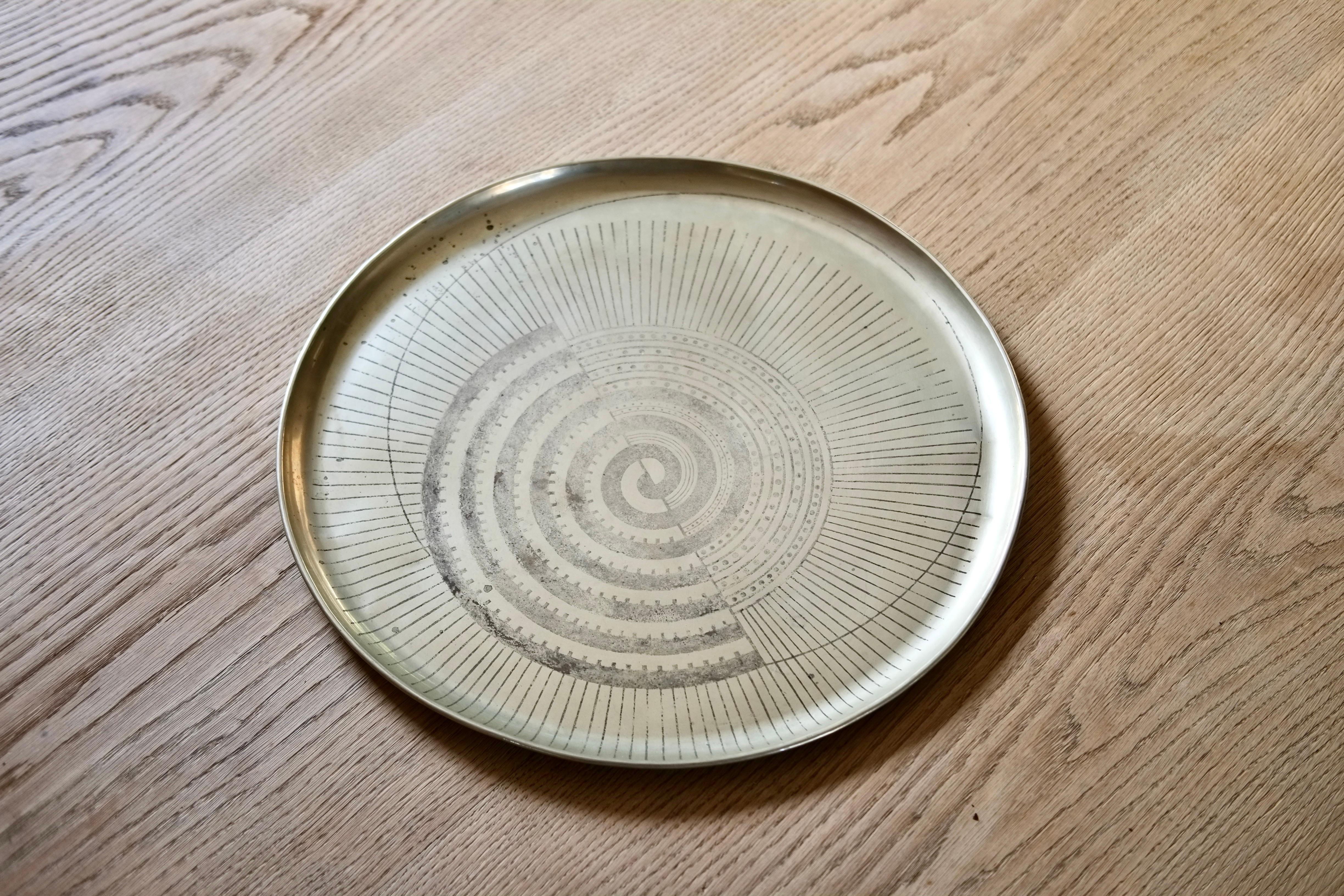 A large circular Dinanderie tray with radiating decoration and spirals by Swiss painter, sculptor and interior designer Jean Dunand (1877-1942), circa 1925. 

Made from patinated nickel silver. The tray has depatinated over the years and has some