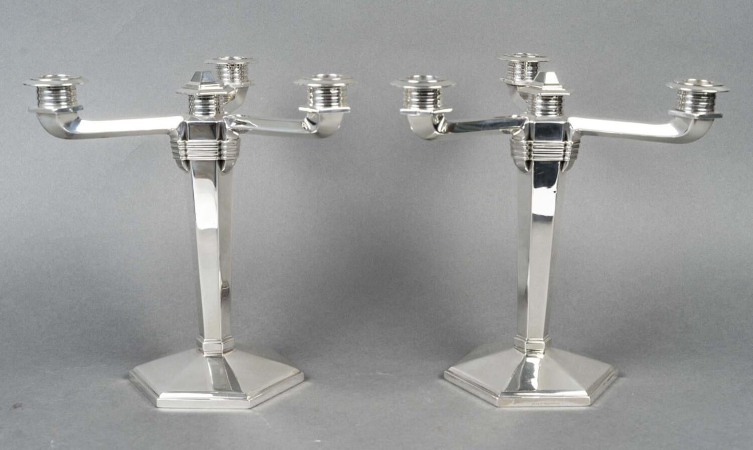 Coppia di candelabri in argento, a base esagonale con sfaccettature triangolari, sormontati da un fusto ad anello, con lati tagliati, da cui emergono tre bracci di luci e al centro un cabochon.

Dimensioni: altezza 26 CM - Interasse 26 CM - Diametro