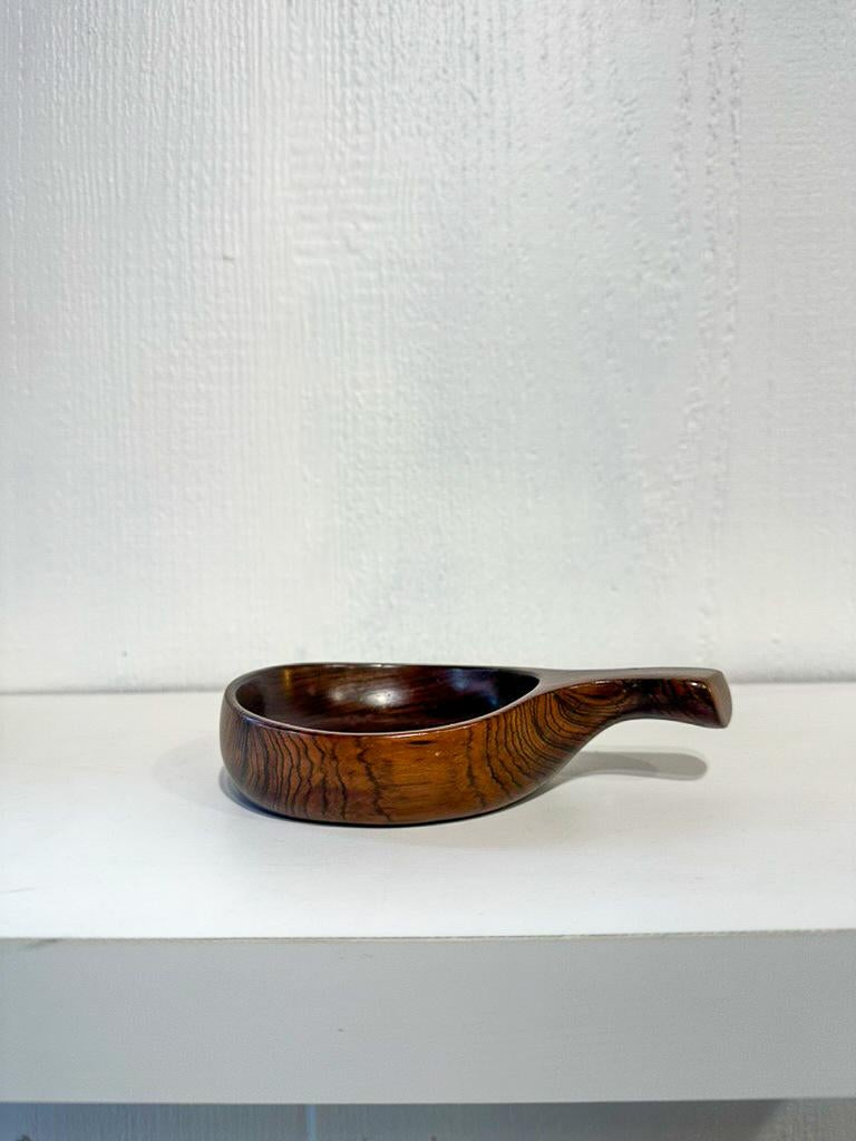 Bol avec anse dessiné par Jean Gillon et produit par Italma/WoodArt, datant des années 1960. Fabriqué en bois massif, ce bol a des dimensions de 16 x 3 x 10 cm, ce qui lui confère une taille compacte et une forme élégante.

La qualité de l'exécution