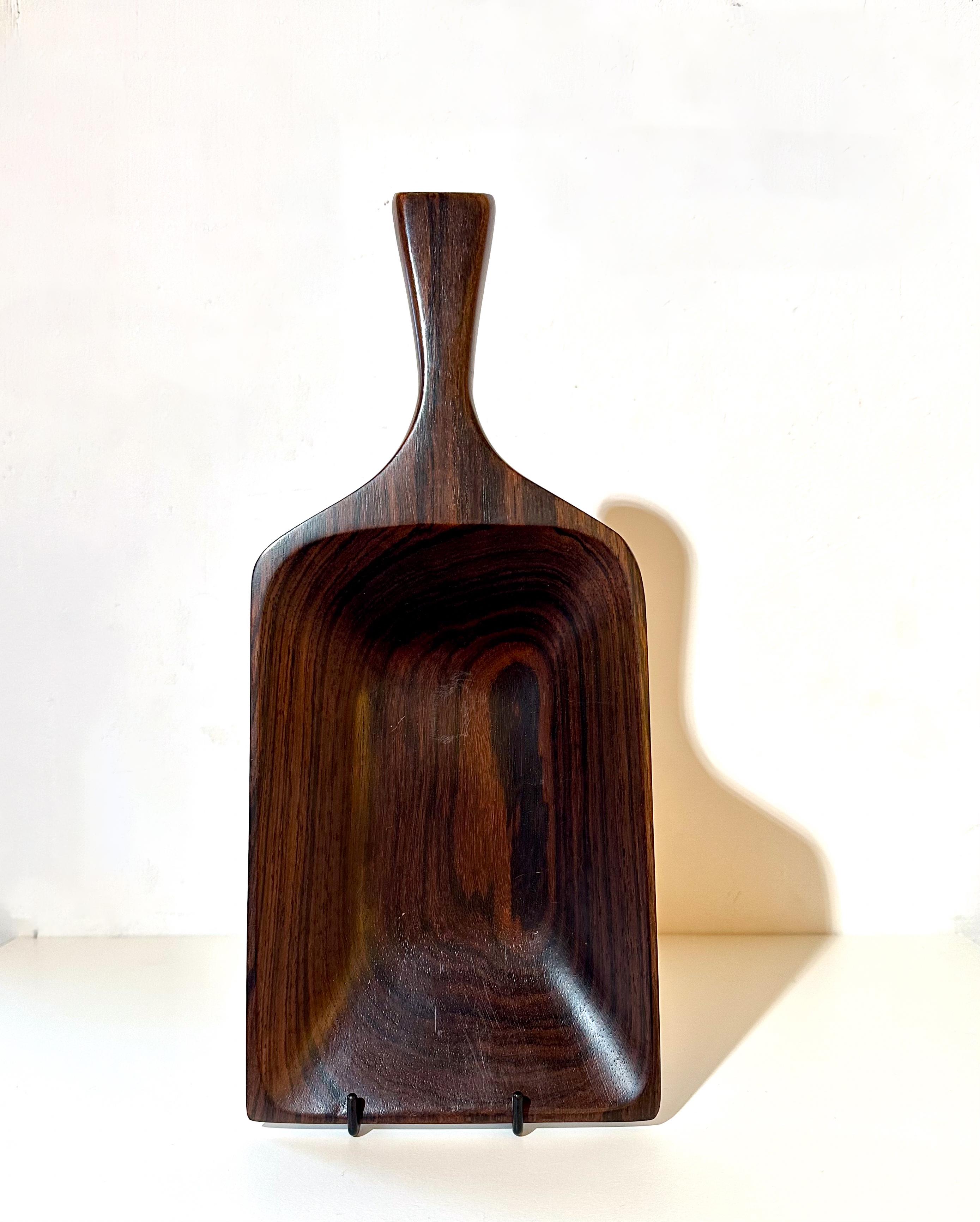 Jean Gillon
Modell 109. ca. 1960
Das Tragen des Wood Art Labels
MATERIAL: Massivholz
Abmessungen: 35 x 14,5 x 4 cm

Dieses außergewöhnliche Tablett, das um 1960 von Jean Gillon entworfen wurde, zeichnet sich durch seine elegante, an eine Schaufel