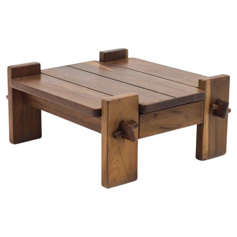 La table basse dessinée par Jean Gillon est une pièce remarquable en bois massif, avec un épais plateau amovible aux découpes carrées dans les angles. Cette caractéristique ajoute une touche de sophistication au design minimaliste de la table.

Les