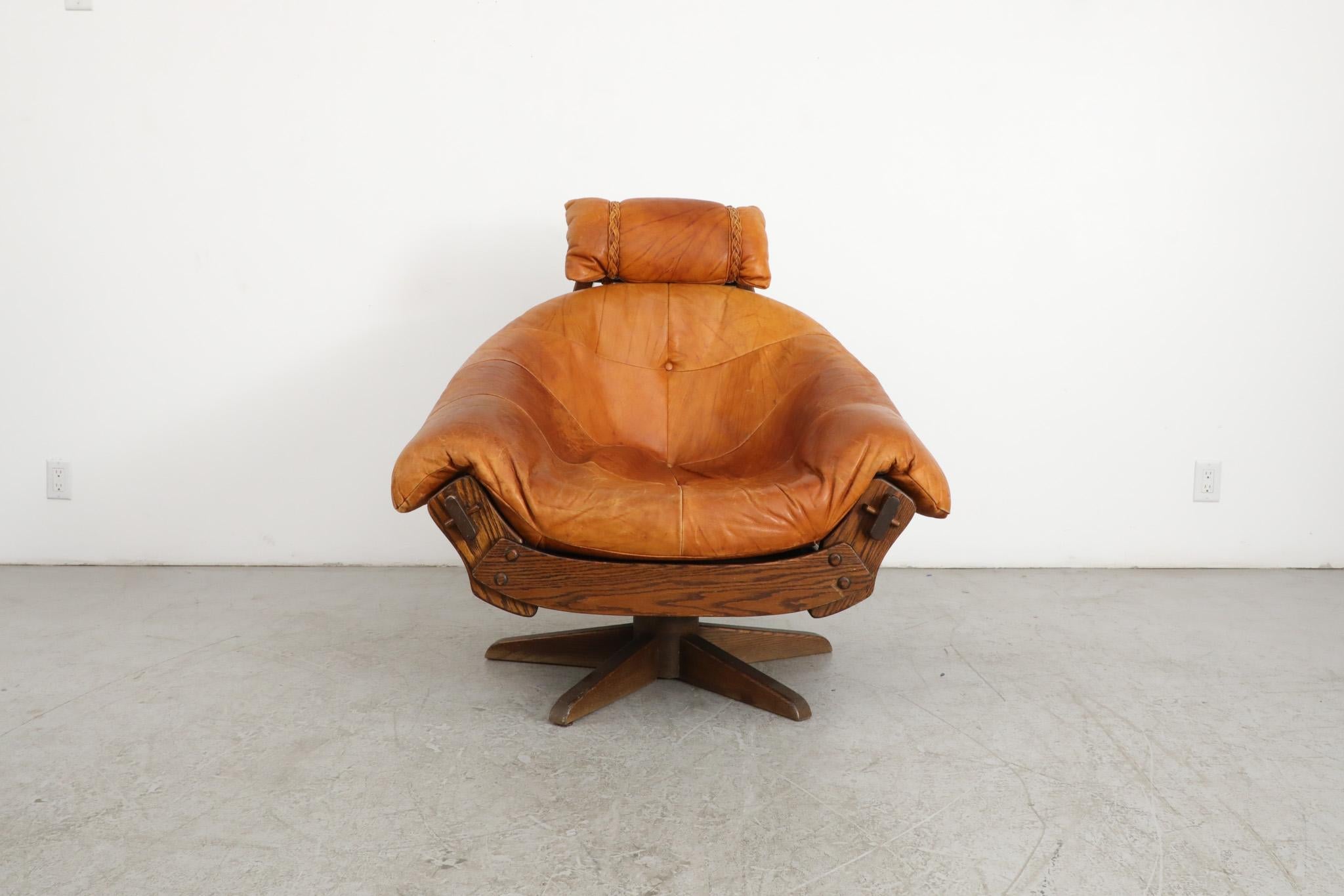 Handsome mid-century Jean Gillon style swivel lounge chair with cognac leather cushions on a Brutalist natural oak wood frame. A striking and stylish statement piece lounge with lovely patina and attractive grain pattern. In original condition with