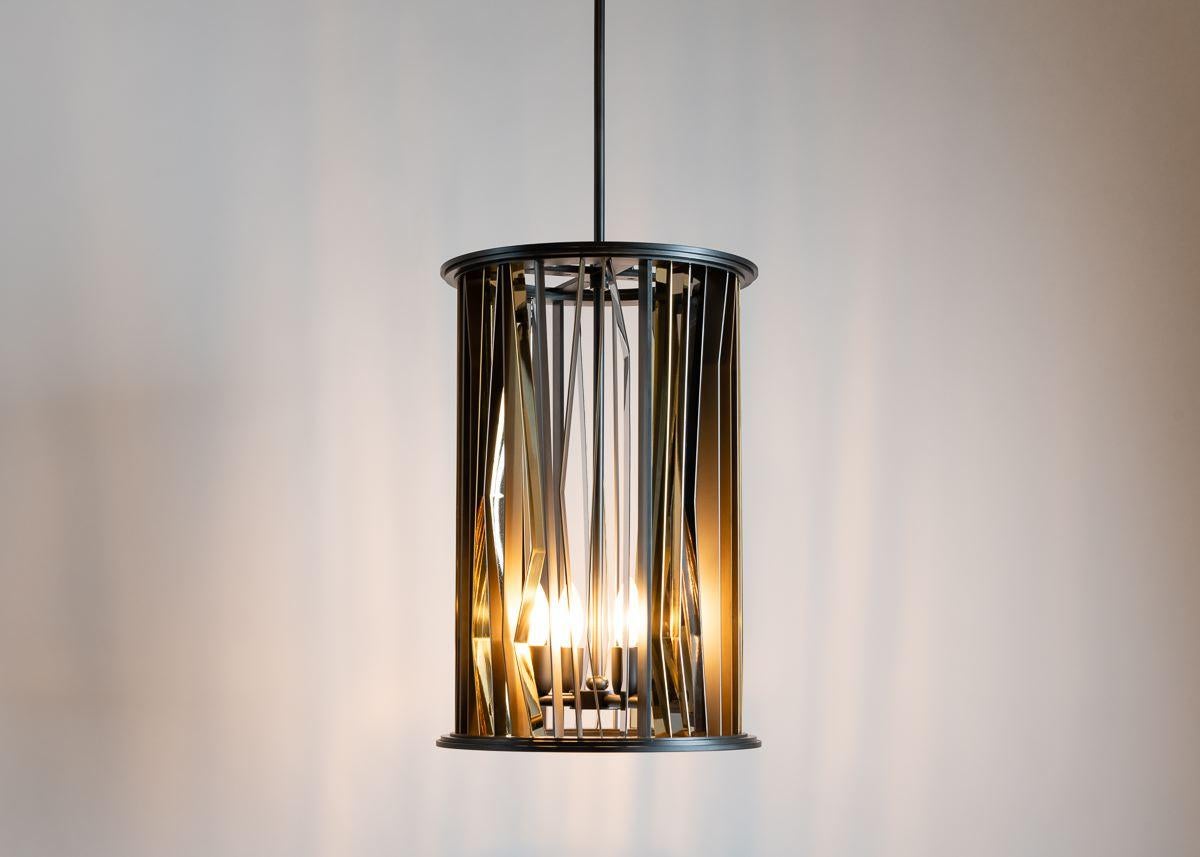 This pendant, available in three sizes—the largest an ellipsis, the two smaller sizes cylinders—is made of gunmetal steel alternately patinated or polished to a satin soft finish. The gleaming brass strips that adorn the chandelier pay tribute to