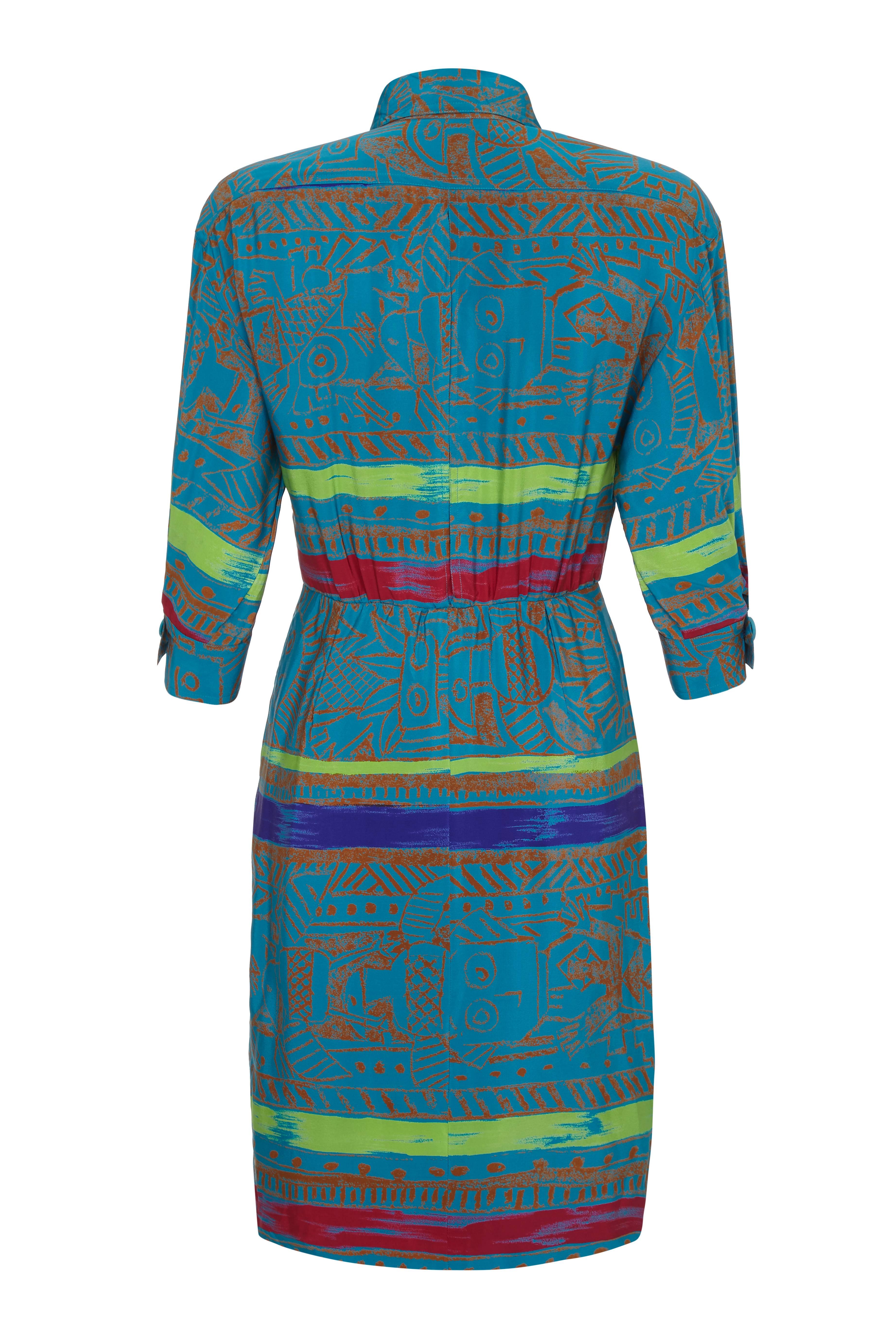 This vibrant 1980s colourful batik style printed silk shirt dress by Jean - Louis Scherrer is in excellent condition and has a dynamic modern aesthetic. The majority of the print is a deep turquoise, and features horizontal bands of colour in lime