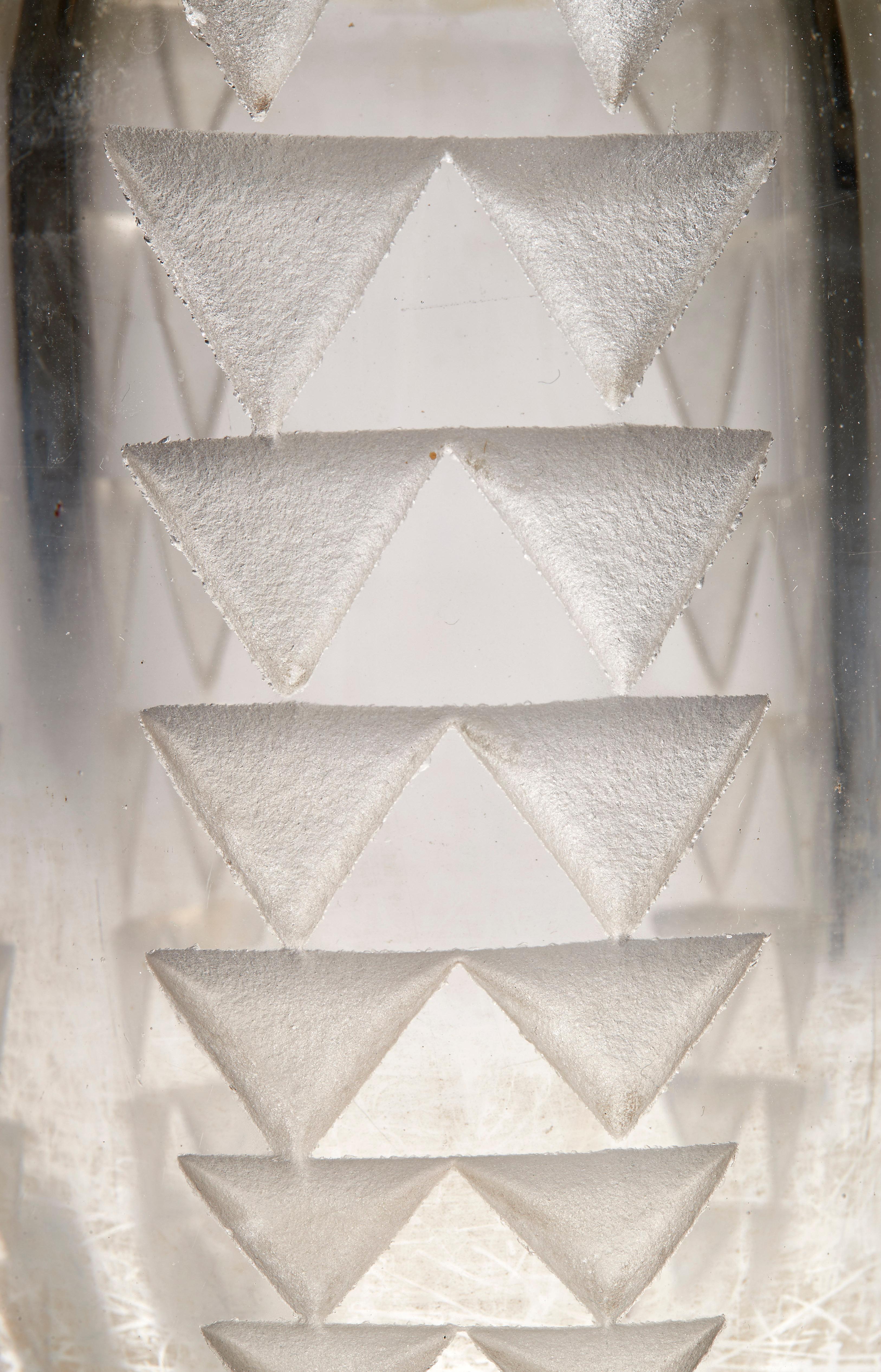 Petit vase cylindrique en verre épais translucide, décor géométrique de frises verticales à motifs triangulaires décroissants gravés à l'acide. Signature du monogramme de l'artiste sous la base.

Bibliographie :
René Chavance, Les verreries de
