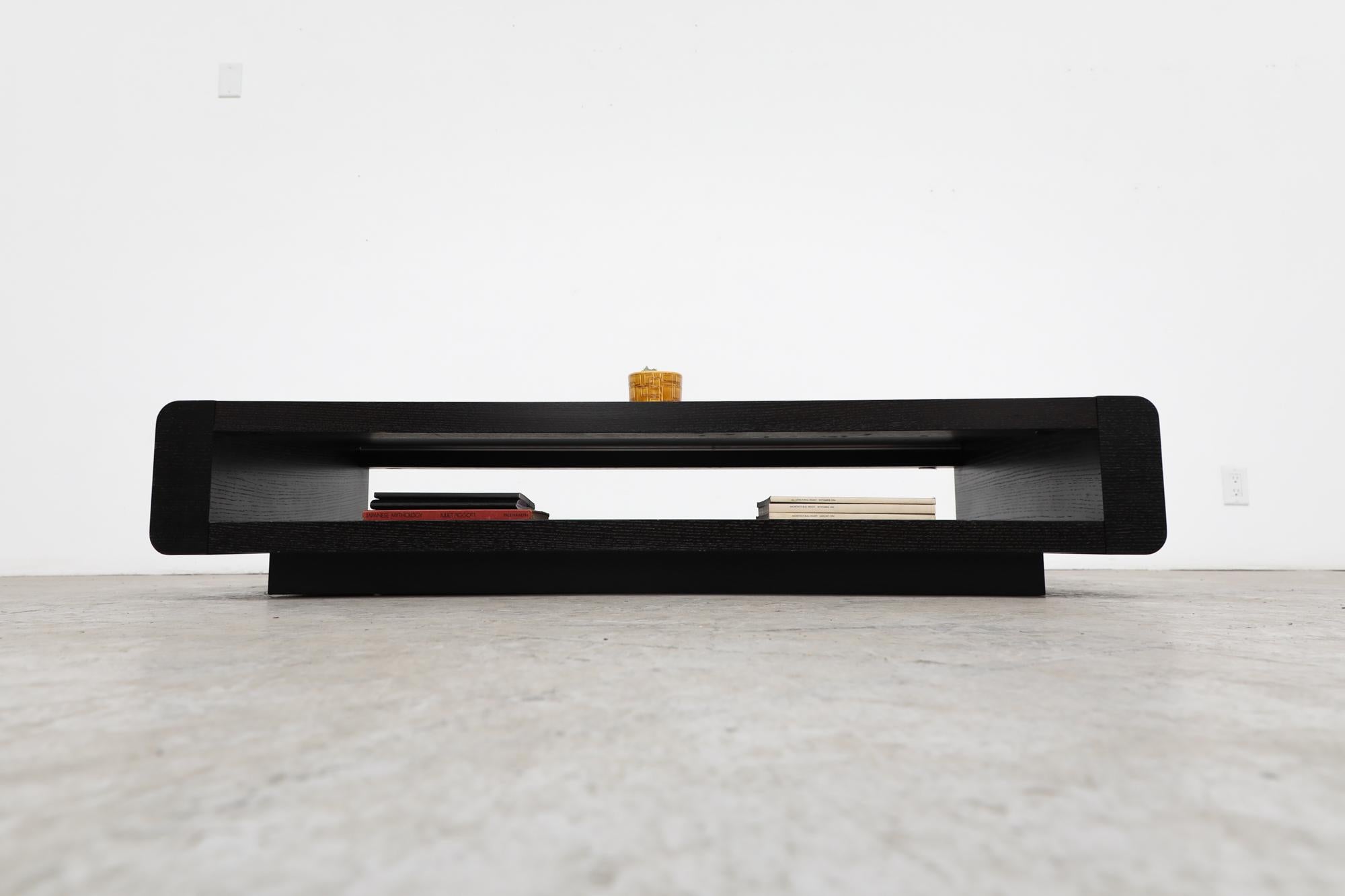 Maneval style low and stealth 1970's dark wenge coffee table with inset black back painted glass top and lower magazine and book shelf. In original condition with visible wear, including heavy scratching to the black glass. Wear is consistent with