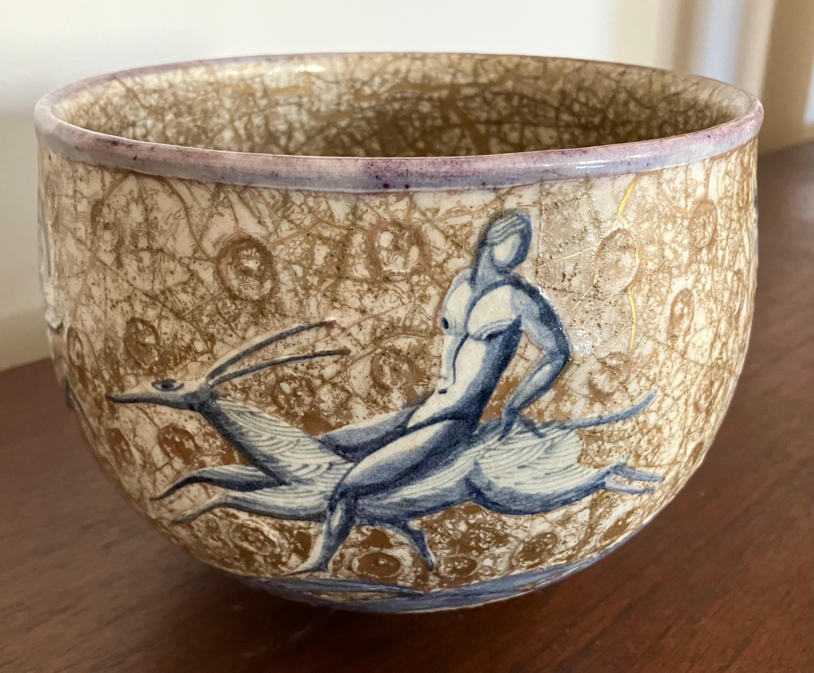 Elegant and atmospheric design by legendary French Art Deco ceramicist Jean Mayadon. Blue and white nude male and female figures riding stylized gazelles encircle the bowl, on a mottled brown and gilt craquelure ground. A striking design