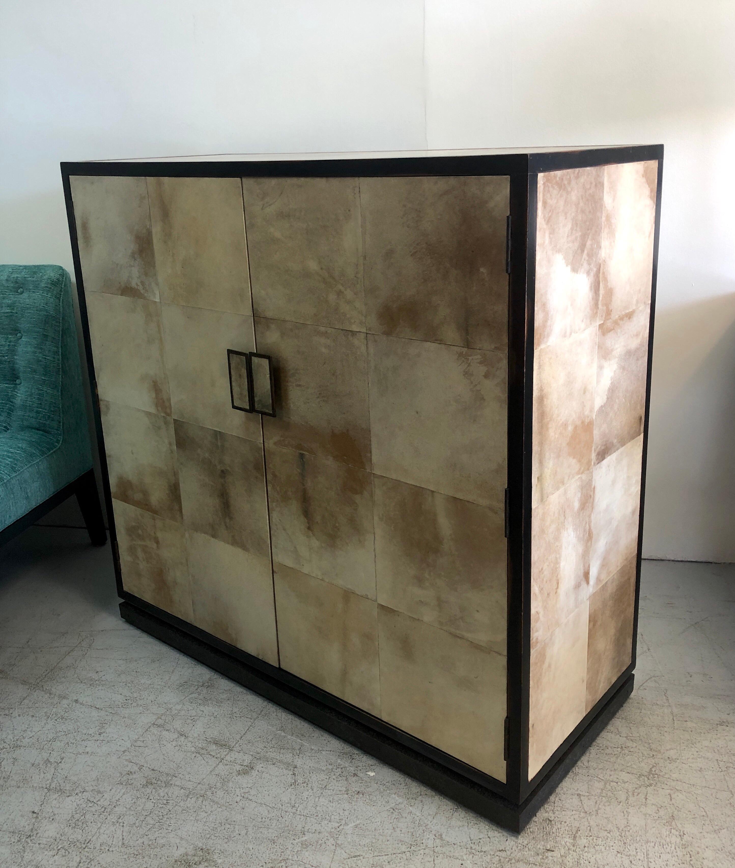A Jean Michel Frank style console, bar or cabinet. Parchment on sides, top and front of doors. The interior features an adjustable shelf. Bronze pulls and base. The wood frame is ebonized and shows intentional distressing.
