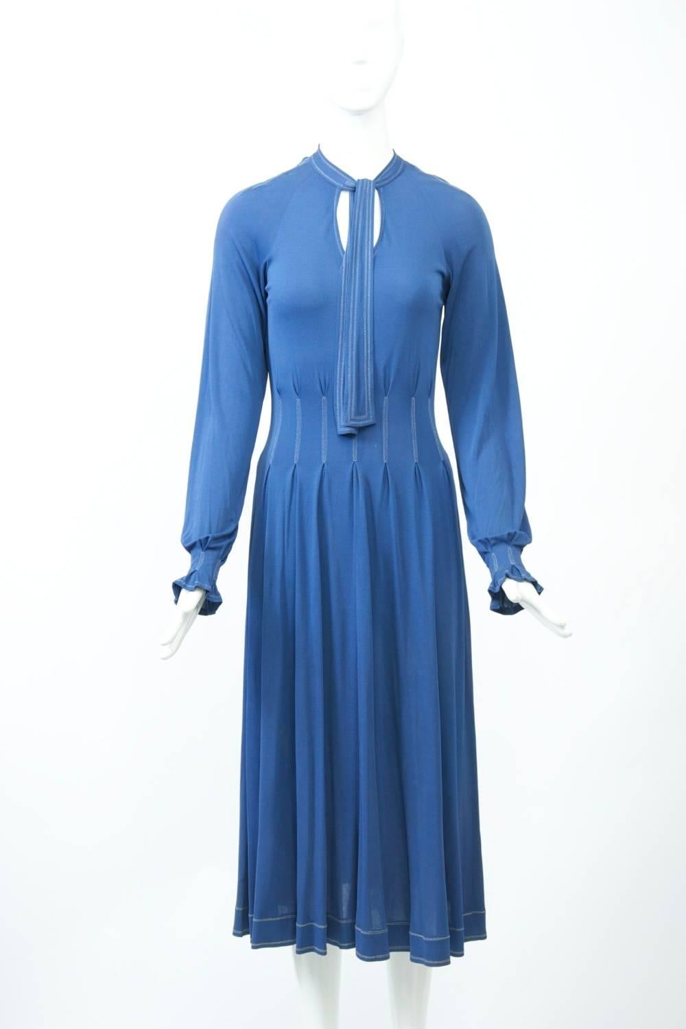 Jean Muir steel blue dress, c.1979s featuring her characteristic details - matter jersey fabric, contrasting stitching, and tie neckline. On this example, the waist area has interval pleating accented with the white stitching that highlights the