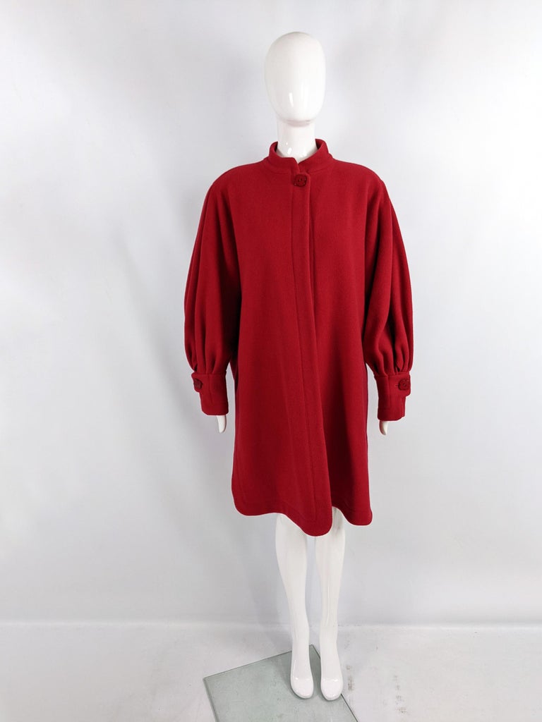 A fabulous vintage womens coat from the 80s by iconic British fashion designer, Jean Muir. In a red wool fabric with a single button flower button at the neck and one on each cuff. It has an open front from the neck down, shoulder pads and pleated