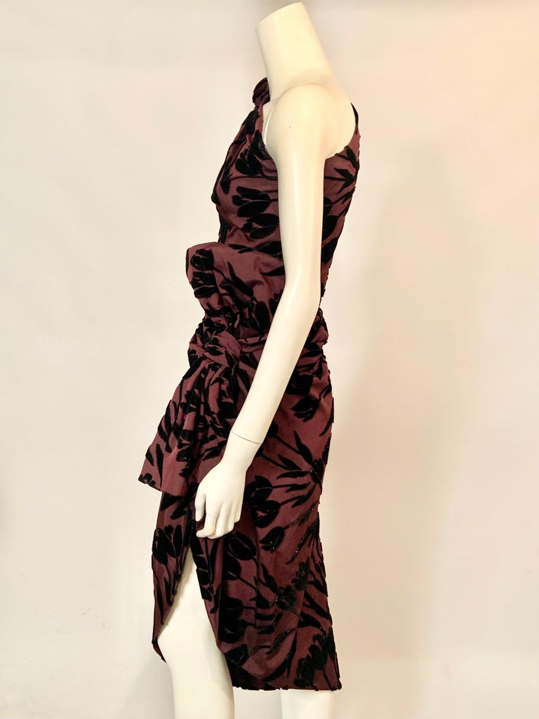 This stunning one shoulder, draped silk dress from Jean Patou has an aubergine silk background with black velvet tulips blooming everywhere.  There is a gathered fabric flower on the right shoulder, a side zipper, and a large bow and drape on the