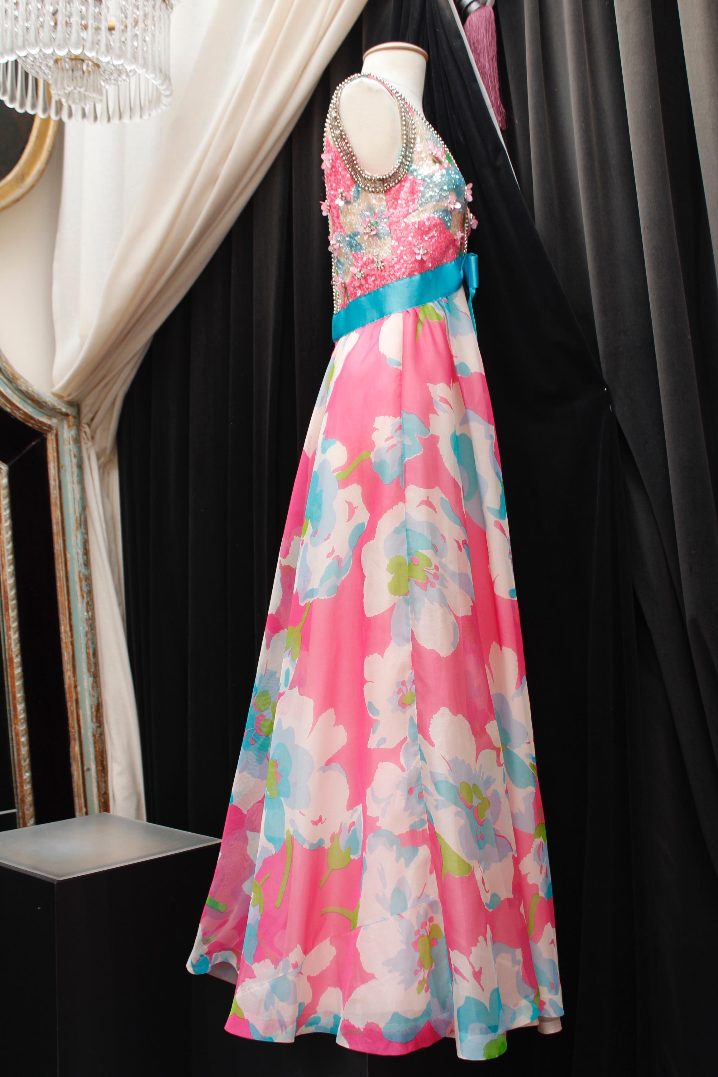 JEAN PATOU BOUTIQUE – Lovely sleeveless dress, composed of silk taffeta with floral pattern in pink, white, green and blue colors. It features a V-neck, a belt with a turquoise bow, and a bust entirely embroidered with sequins and beads in matching