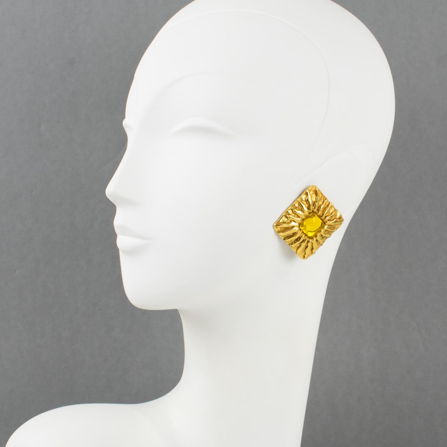 These lovely Jean Patou Paris signed clip-on earrings feature a square, gilt metal shape with a carved sun pattern. They are embellished with a bright yellow Gripoix poured glass cabochon in the center. Each piece is signed with a tag on the