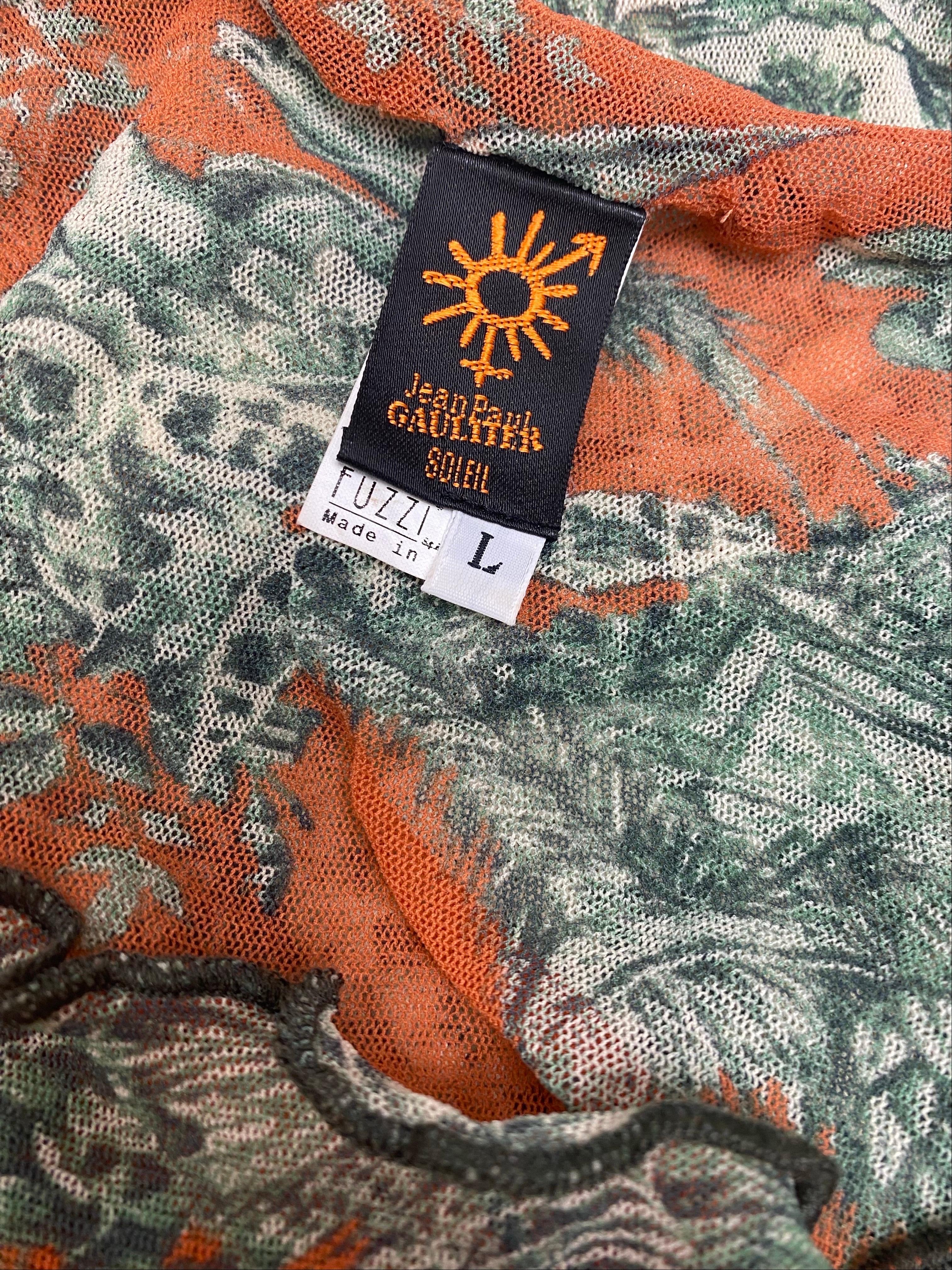 Ce haut en maille Jean Paul Gaultier est un exemple frappant de l'utilisation inventive des imprimés et des textures par le créateur. 
Doté d'un motif classique de Toile de Jouy en vert sur une base de corail doux, ce haut associe des détails