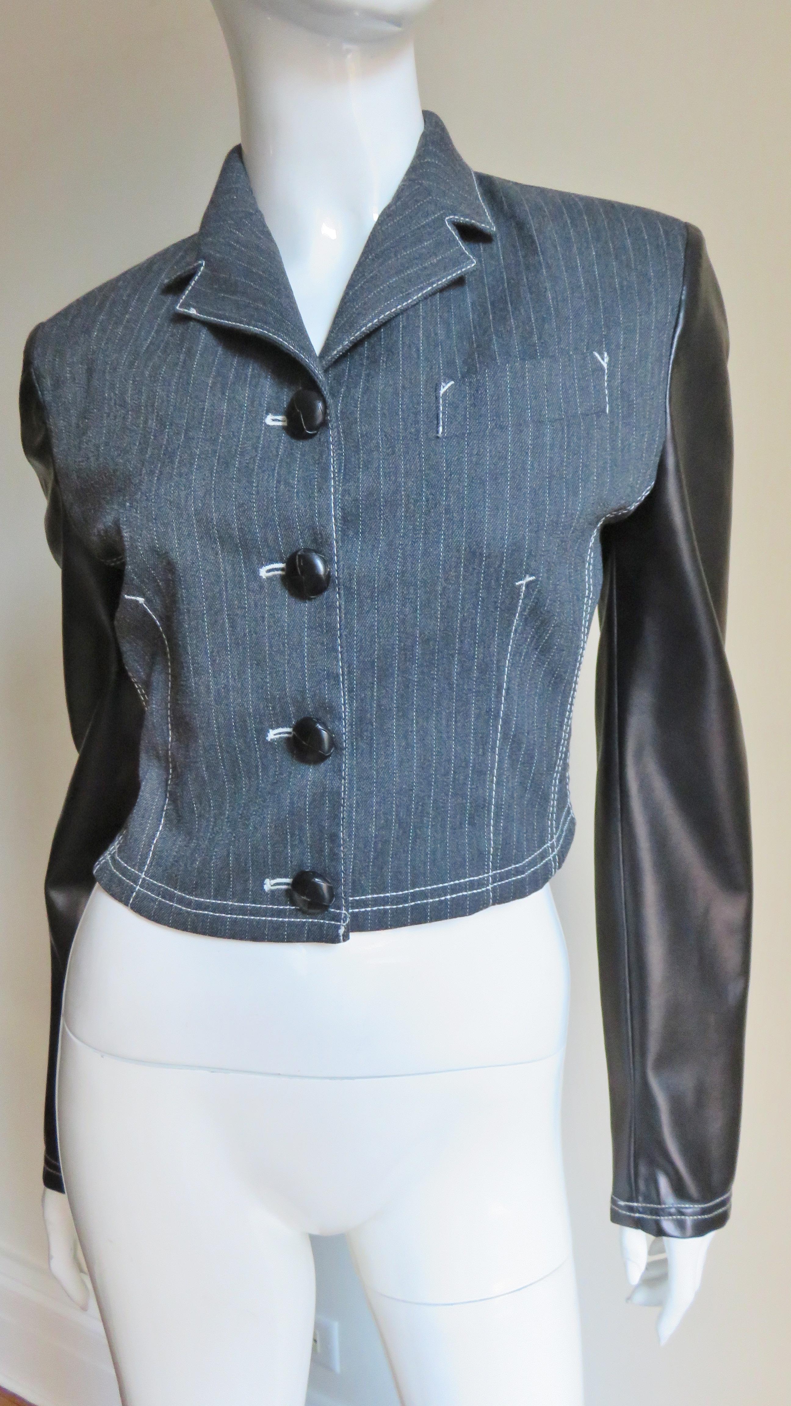 A fabulous cropped jacket from Jean Paul Gaultier's Junior Gaultier line made of grey pinstriped wool and black polyurethane back and sleeves.  It has a small lapel collar, breast pocket, princess seaming and black front buttons.  All seams are