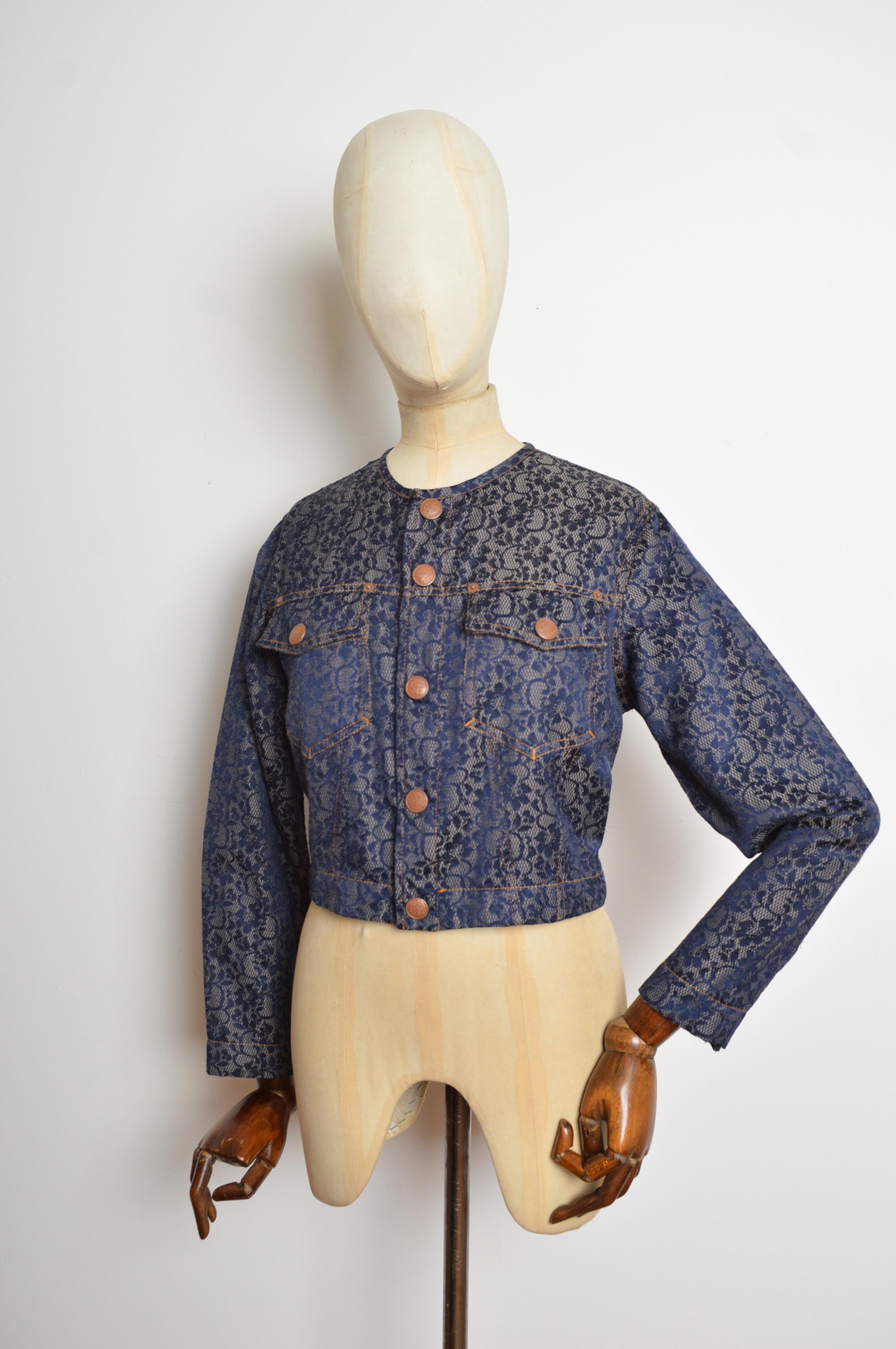 Chaqueta Jean Paul Gaultier intrincadamente decorada con un exterior de jacquard de encaje, botones de cobre con efecto envejecido y bolsillos en el pecho. La chaqueta se puede ajustar mediante lengüetas en la espalda. 1990's.
Talla recomendada;