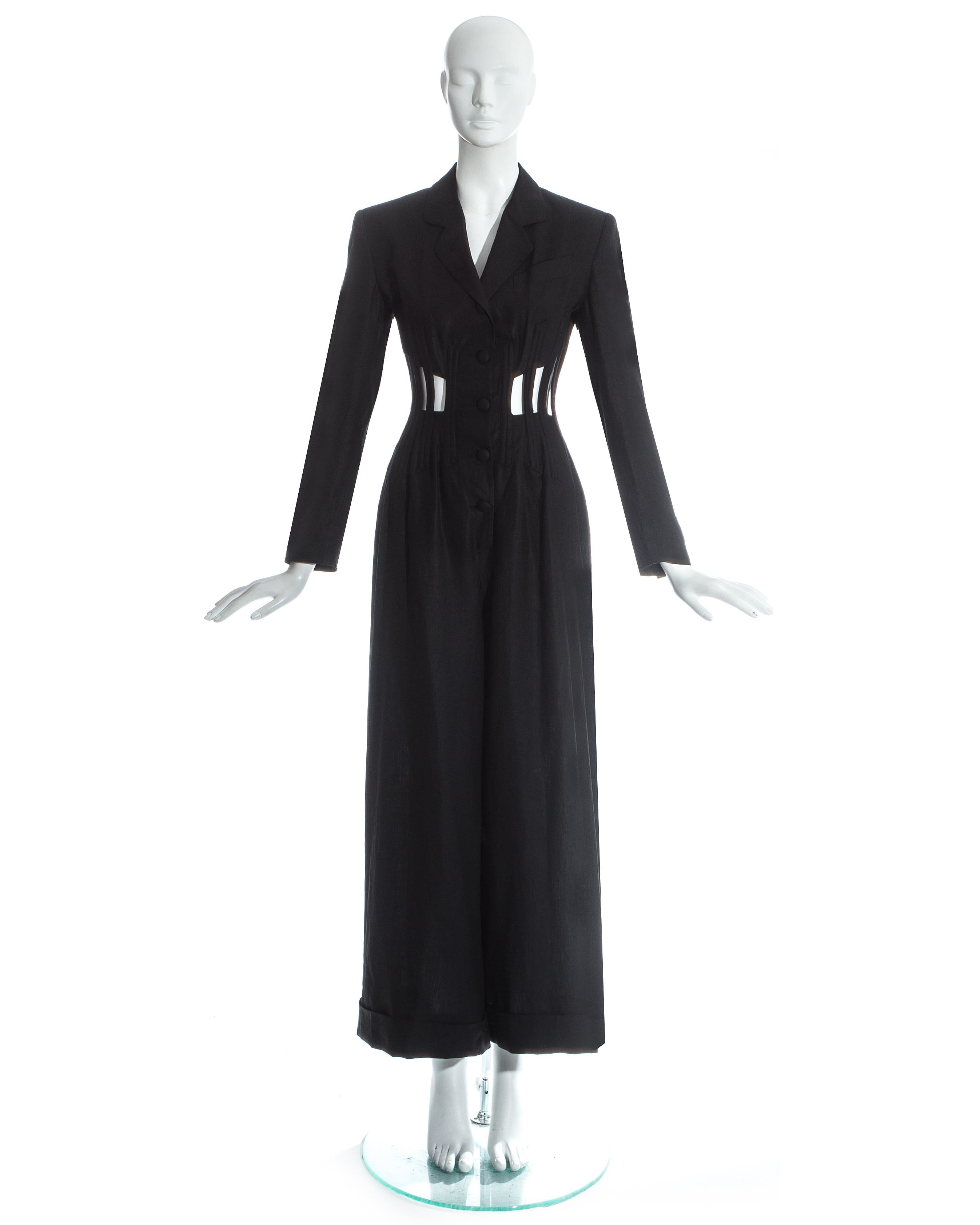 Jean Paul Gaultier; Black linen tuxedo jumpsuit. Caged corset around waist with openings revealing the skin and lace up fastening at the back. Wide leg pants with turn ups, structured blazer with internal padding, and fabric button fastenings at the