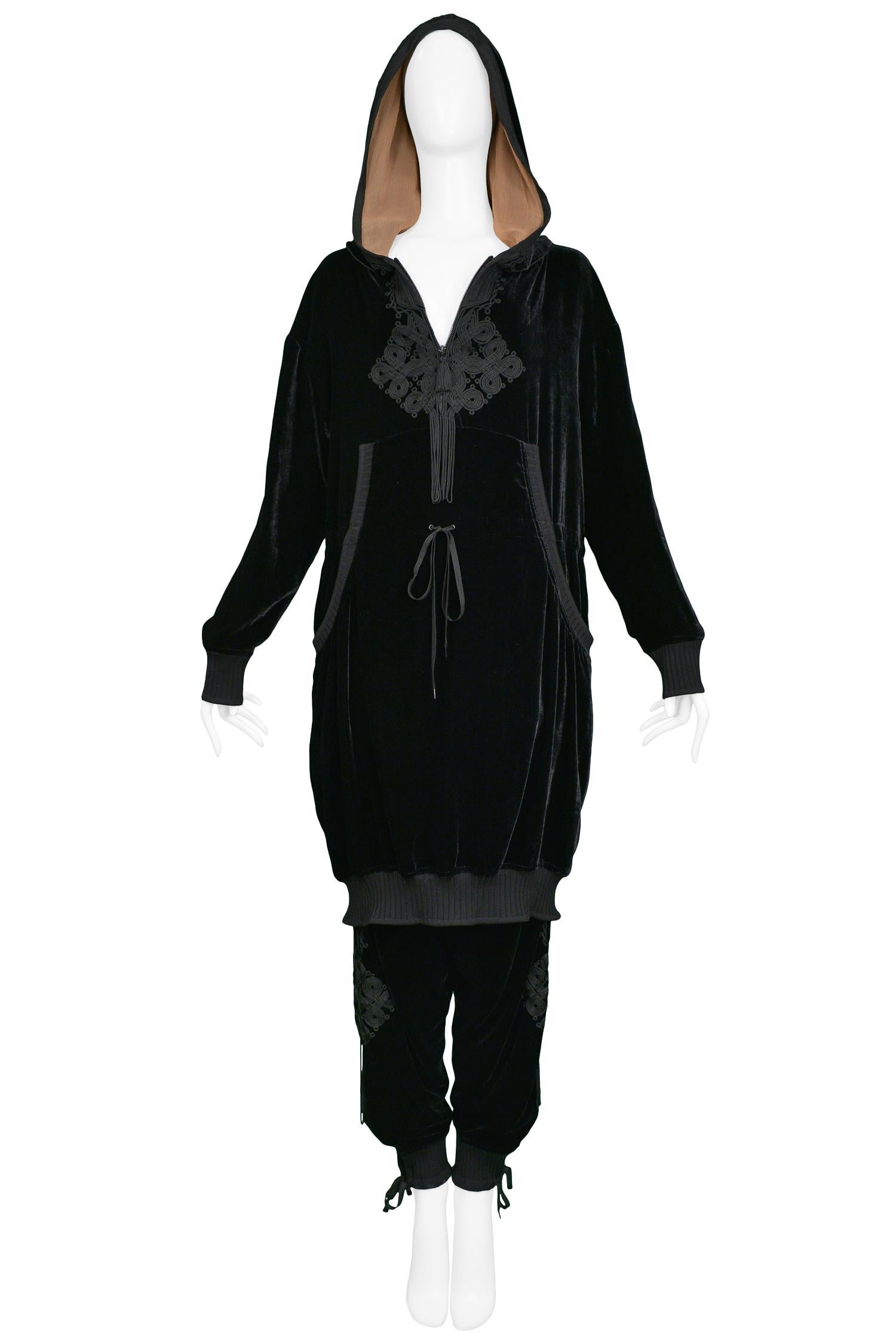 Jean Paul Gaultier black velvet long-sleeve tunic hoodie and matching track pant ensemble. Features black circular trim details and black cord geometric symbol on hoodie and cuffs. Collection AW 2010.

Excellent Condition.

Size 42