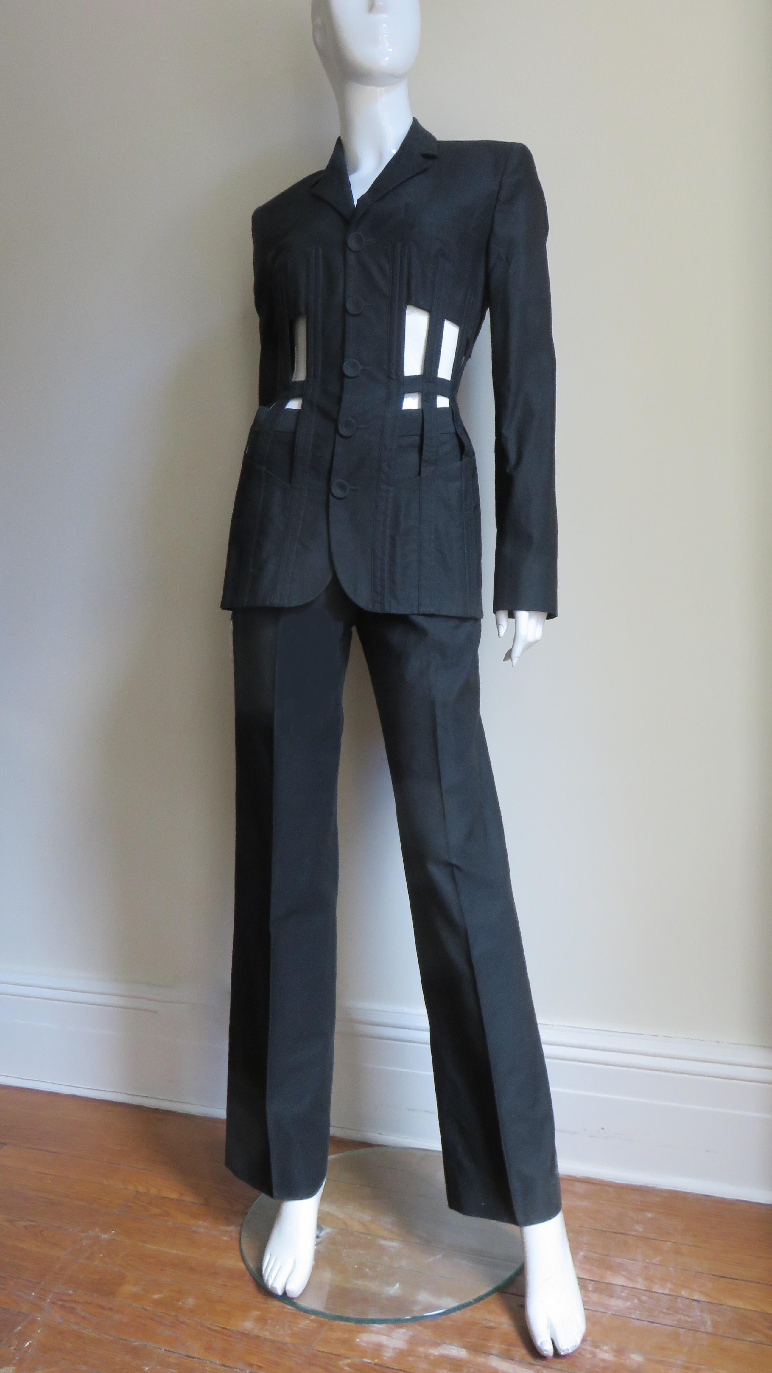 A fabulous iconic black polished cotton lace-up back cage jacket and pants suit from Jean Paul Gaultier Spring/Summer 1989 Collection.  The jacket has incredible vertical boning alternating with cut outs from under bust to hips around the jacket's