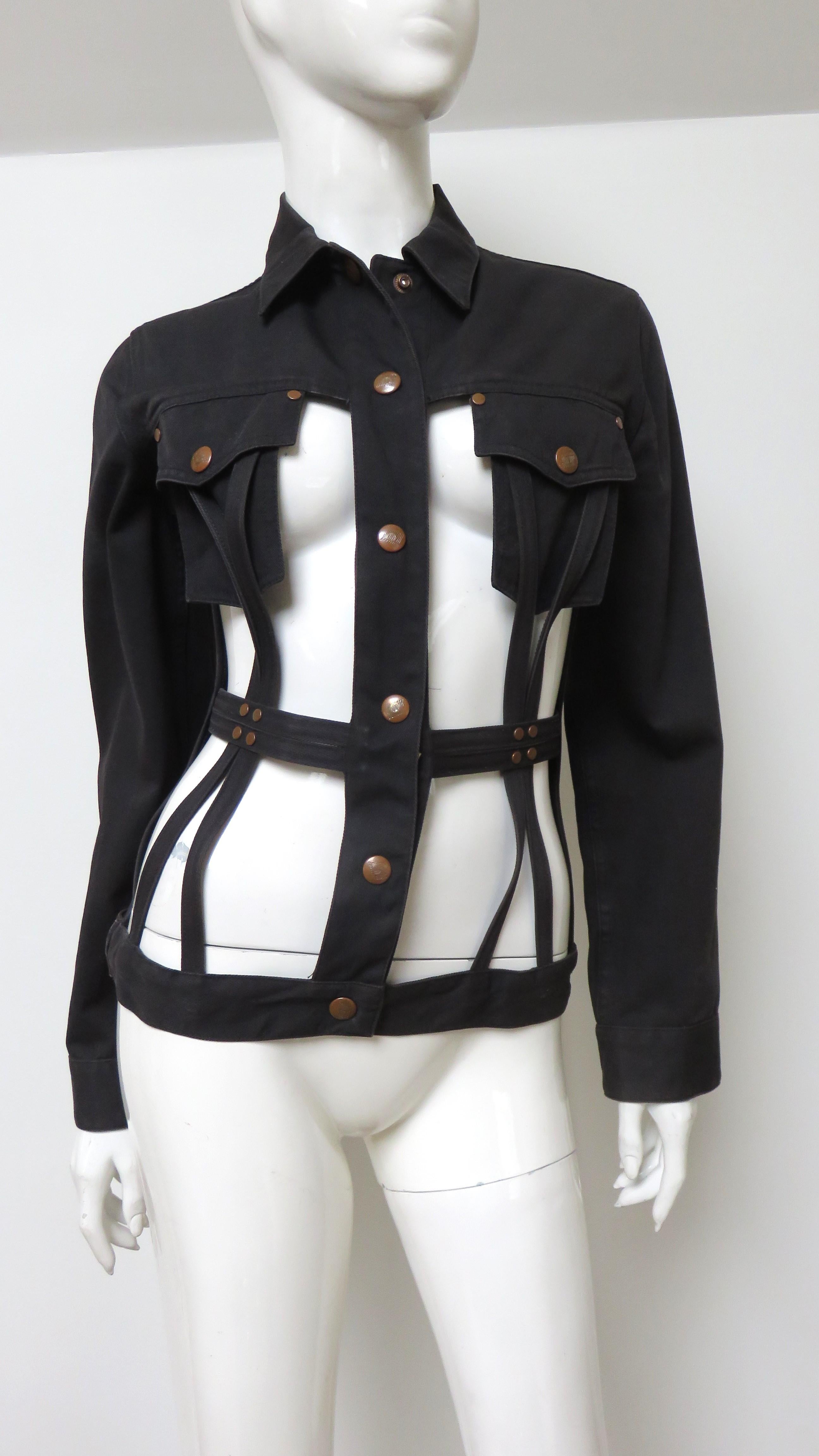 A fabulous black cotton denim jacket from Jean Paul Gaultier's Junior Gaultier line.  It is a take on the jean jacket with the expected long sleeves, collar, yoke and Gaultier inscribed copper metal snaps closing the front, cuffs and breast pockets.