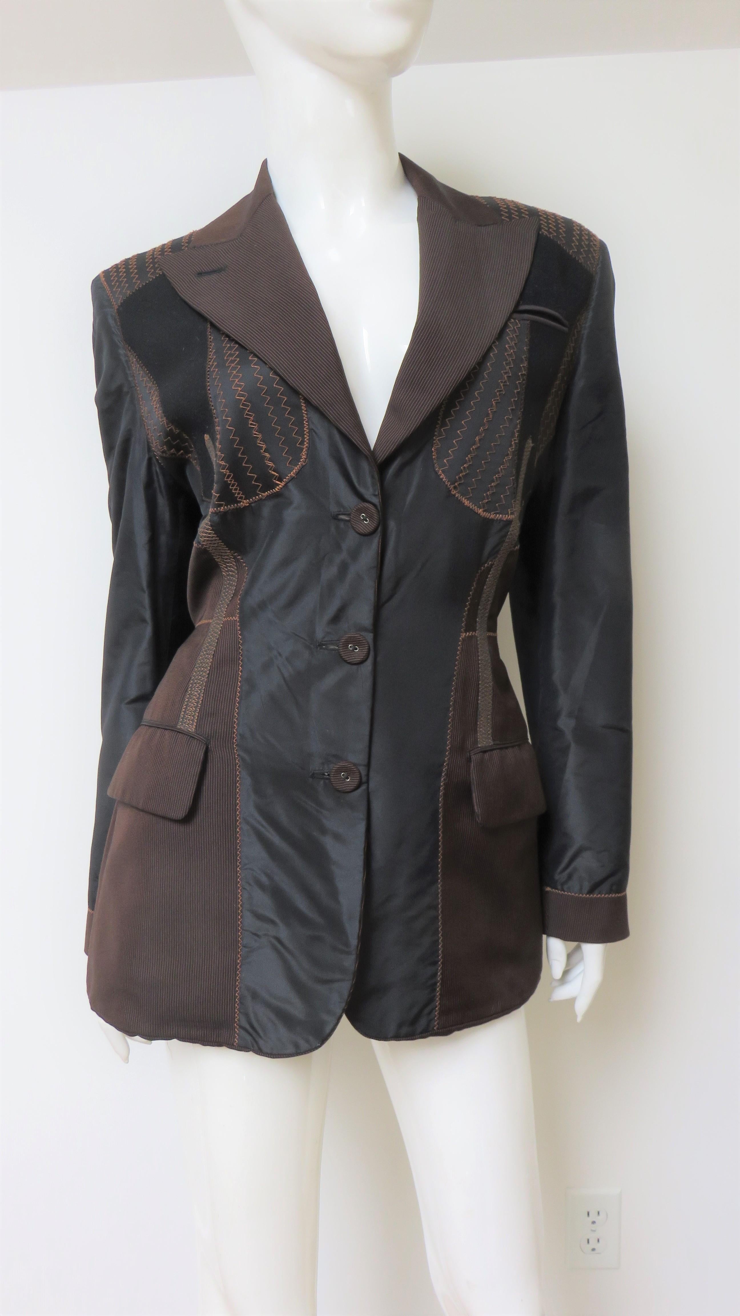 A fabulous silk patchwork jacket from Jean Paul Gaultier.  It is a blazer style jacket with a lapel collar, flap front hip pockets, a welt chest pocket and a button front closure. The front has a brown fine striped collar and sides framing a black