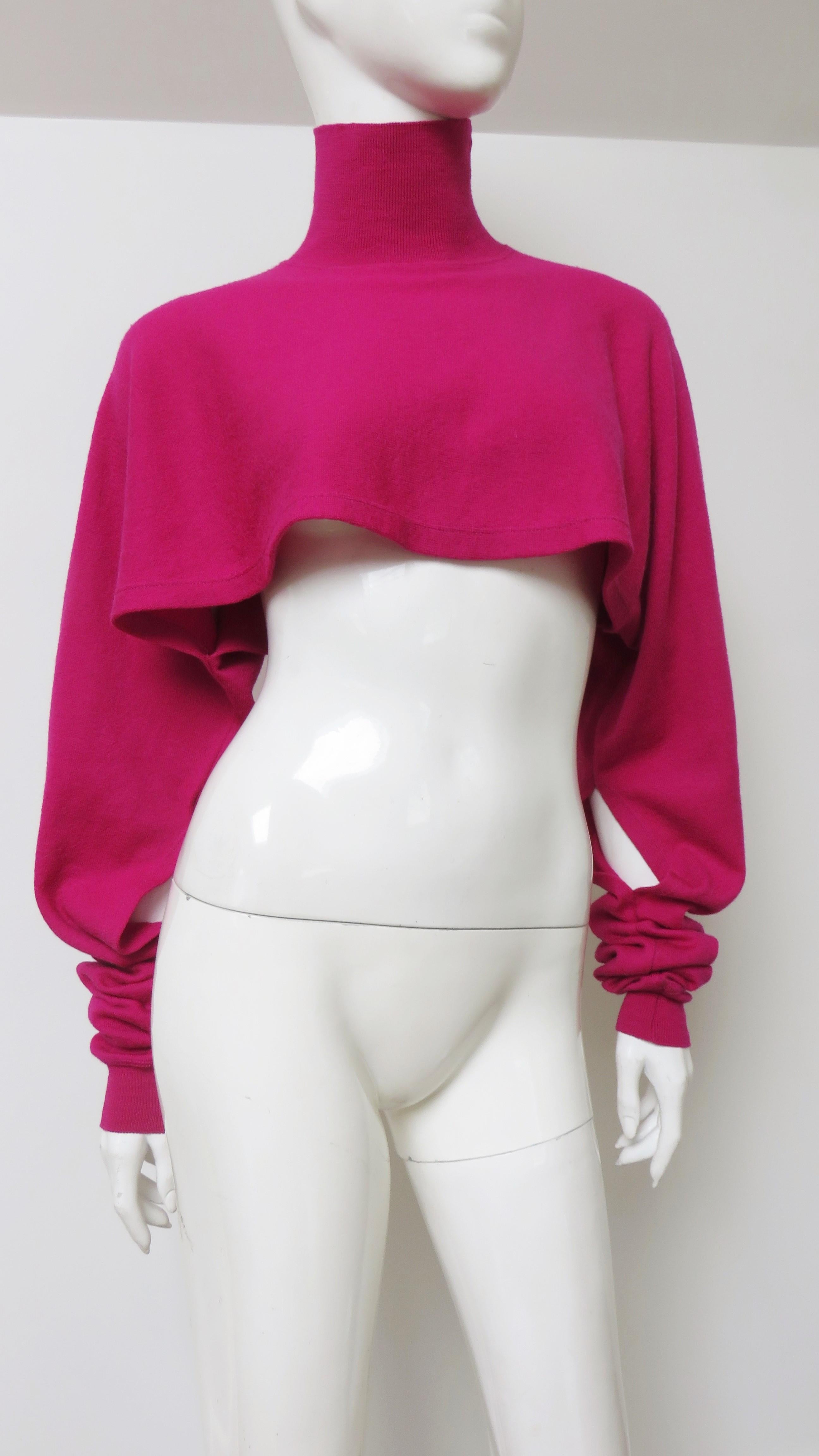 A fabulous bright pink wool cropped sweater from Jean Paul Gaultier.  It has a turtleneck, long cuffed dolman sleeves with cut outs at the inner forearms and a full body cropped just below the bust.  The turtleneck and cuffs are ribbed.
Fits sizes