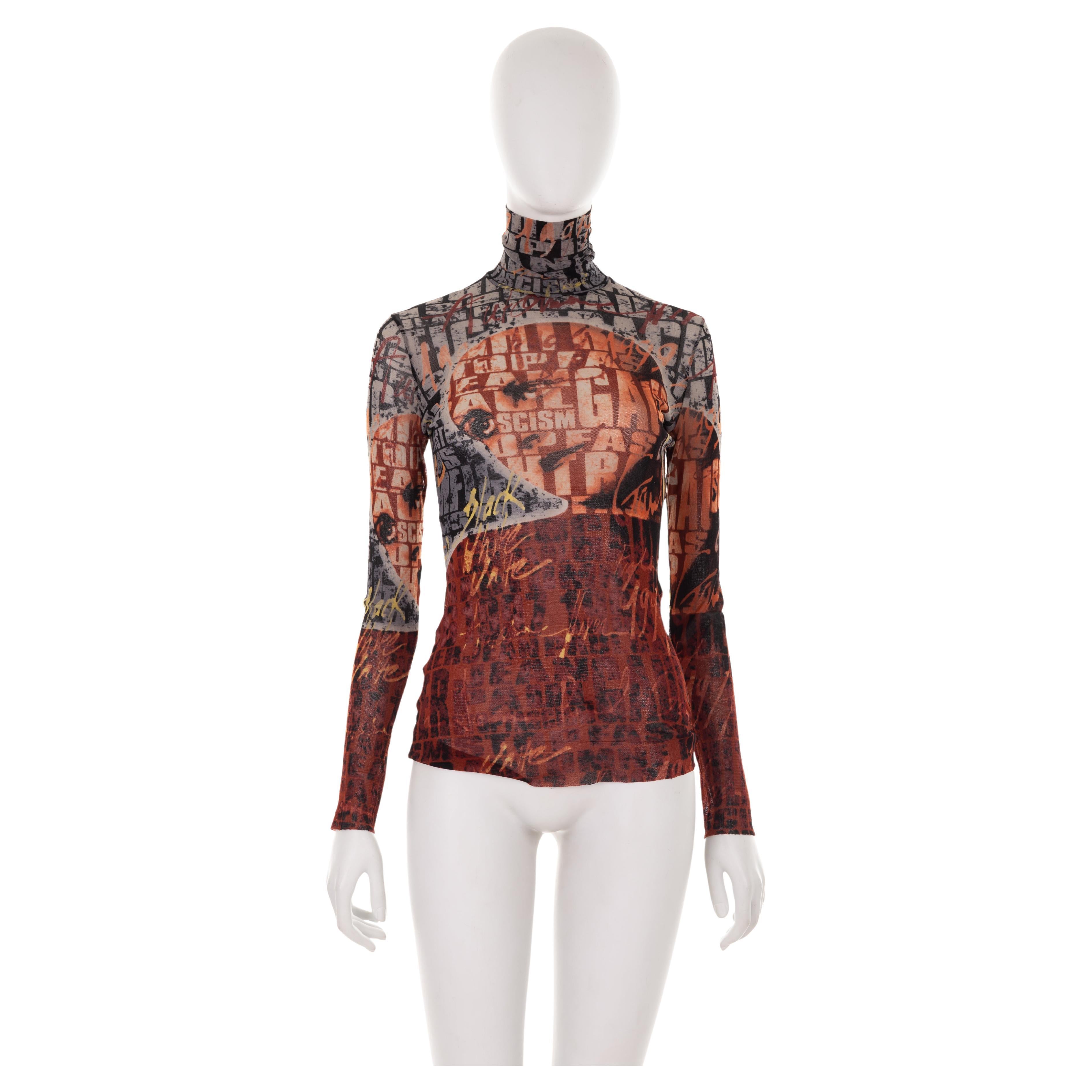 - Jean Paul Gaultier Fall Winter 1997 collection
- Sold by Gold Palms Vintage
- Printed mesh turtleneck top
- Long sleeve
- Portrait print with “Fight Racism” slogan
- Brown/red with grey, yellow, black hues
- Size: M

Shoulder to shoulder: 38 cm/