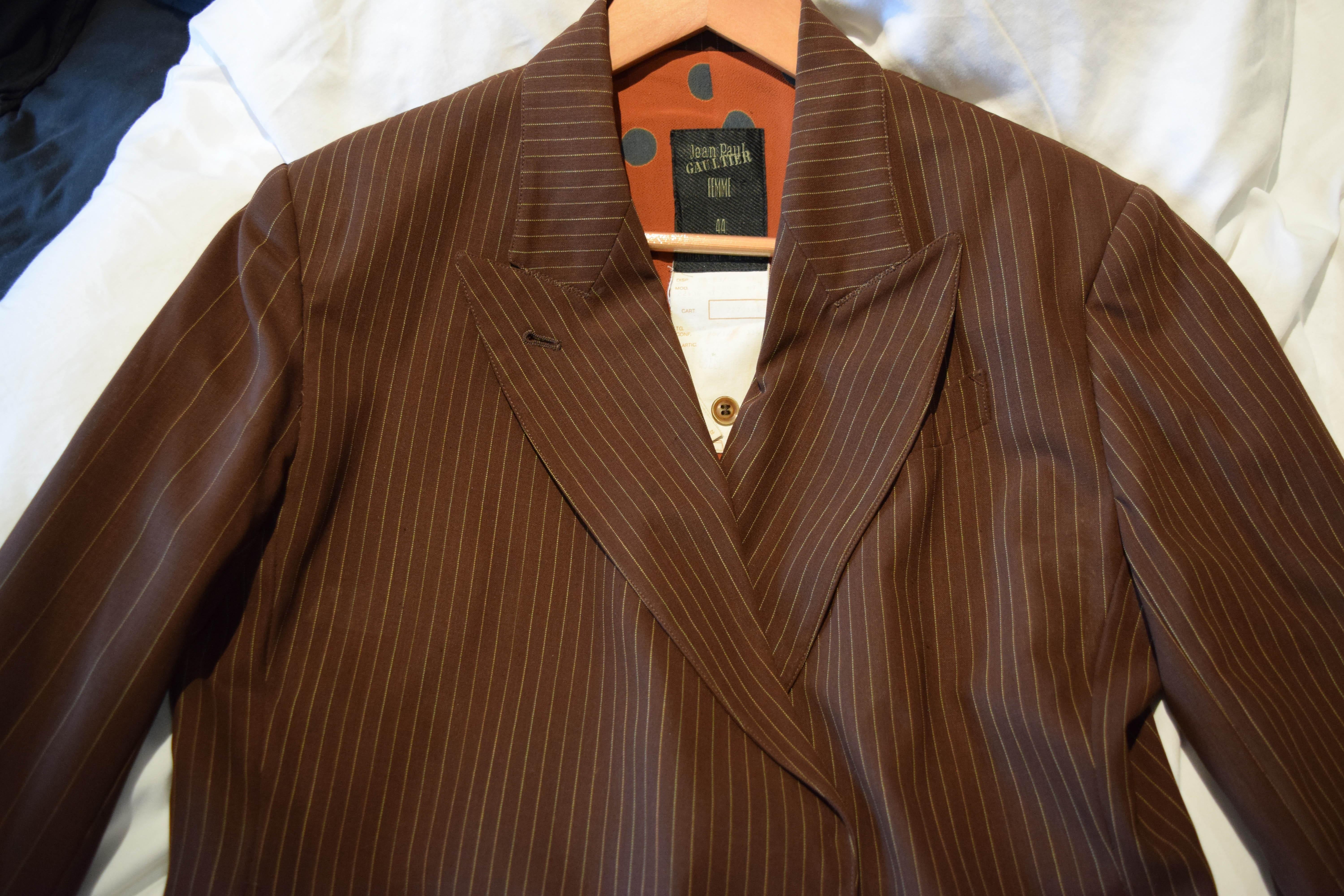 Ecco un bellissimo cappotto lungo da donna di Jean Paul Gaultier.
Strisce sottili marroni sull'esterno del corpo e strisce larghe sulle braccia e sulla fodera interna arancione a pois.  anche un po' sul davanti e all'interno delle tasche