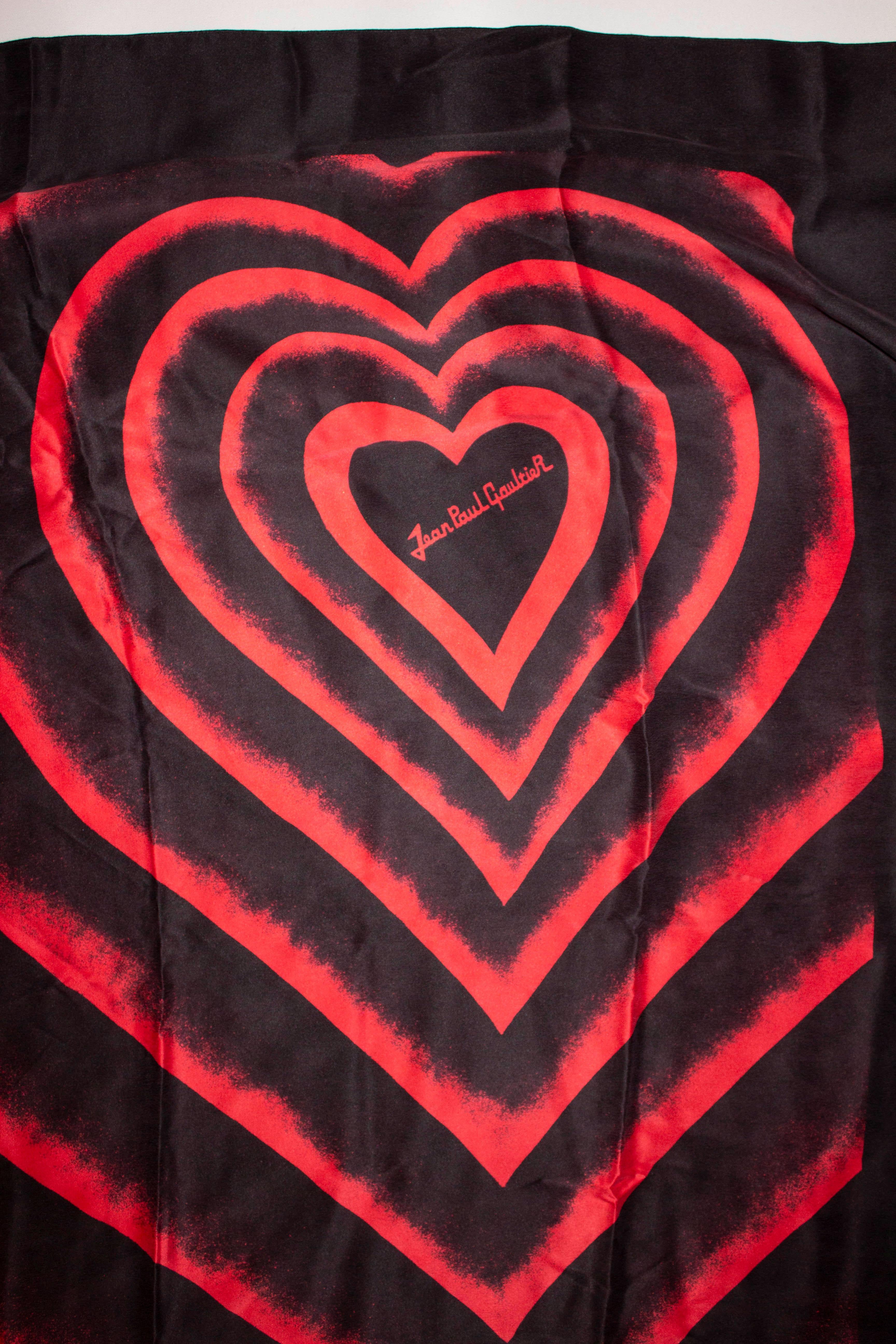 A super soft large silk scarf by Jean Paul Gaultier. The scarf has a black background with a red heart design . It is made in Italy and measures 37'' x 38''