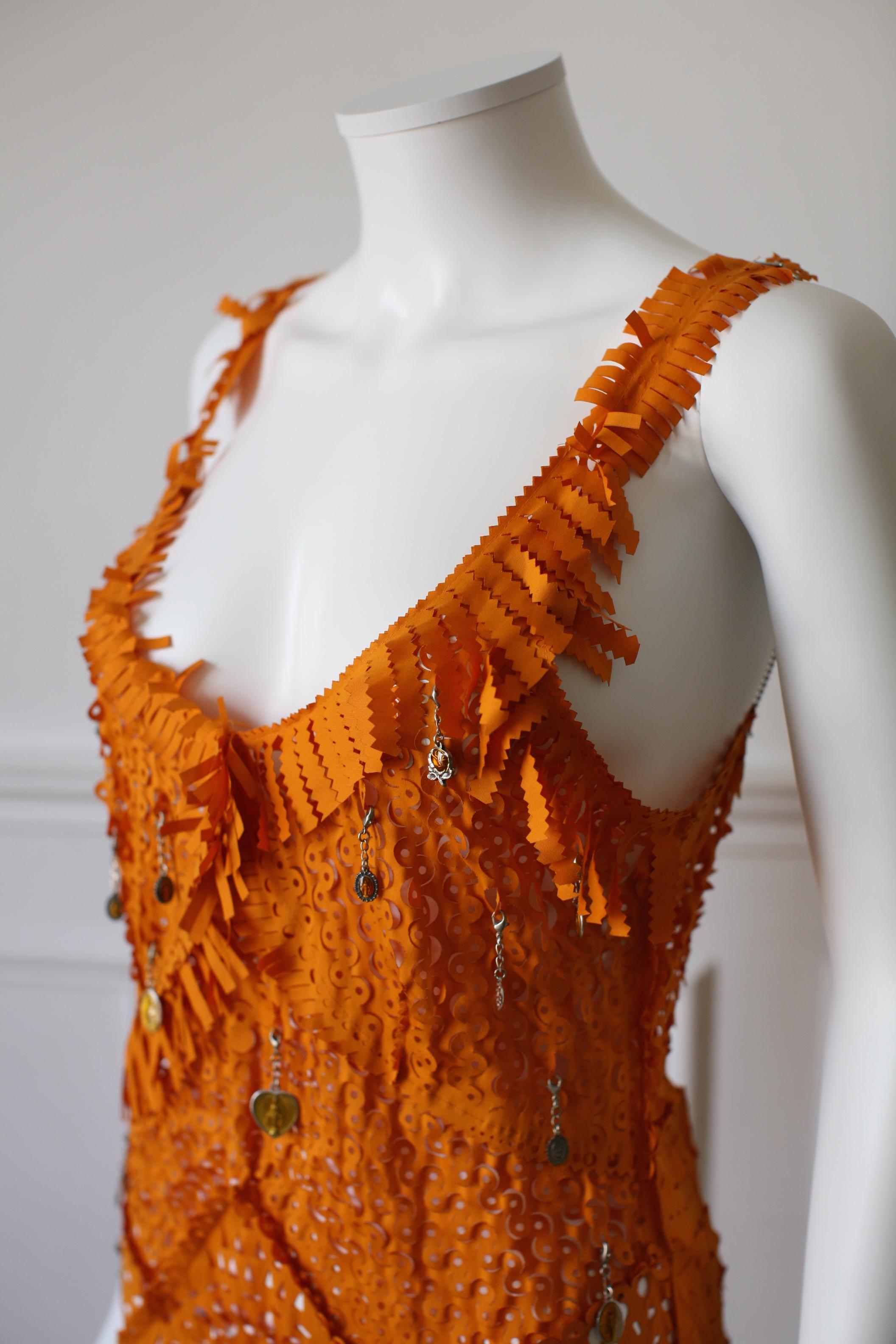 JEAN PAUL GAULTIER, Made in Italy, circa 00’s. Superb orange cotton dress with various patterns cuts in the fabric. Small religious medals are hung randomly and can be moved. The thin metal straps chains can be adjusted. There is a lacing in the
