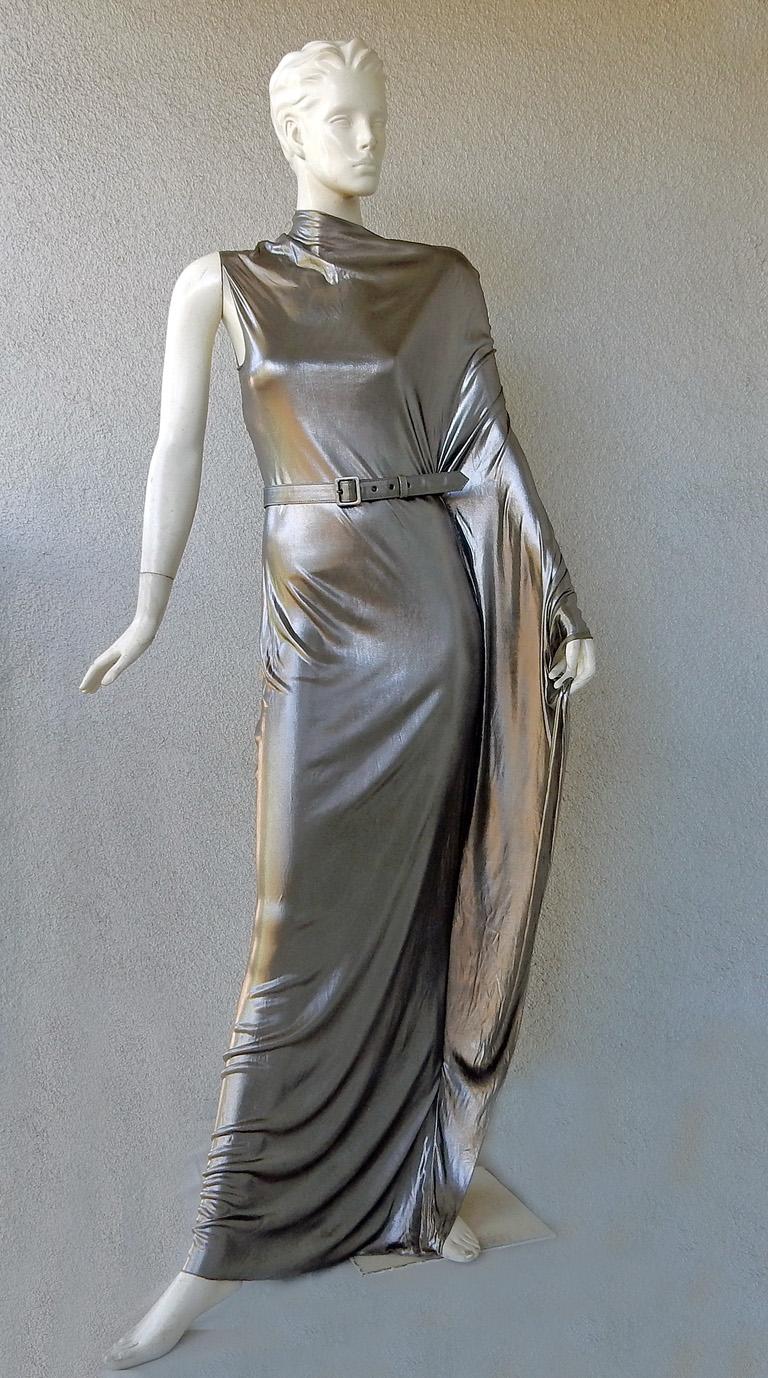 Jean Paul Gaultier Pasarela 2011, estilo 27, vestido de un hombro con cinturón de peltre líquido greco.  El vestido parece de plata brillante con la luz adecuada. Se ciñe fácilmente al cuerpo con una abertura a la altura del muslo.  Cuello falso con