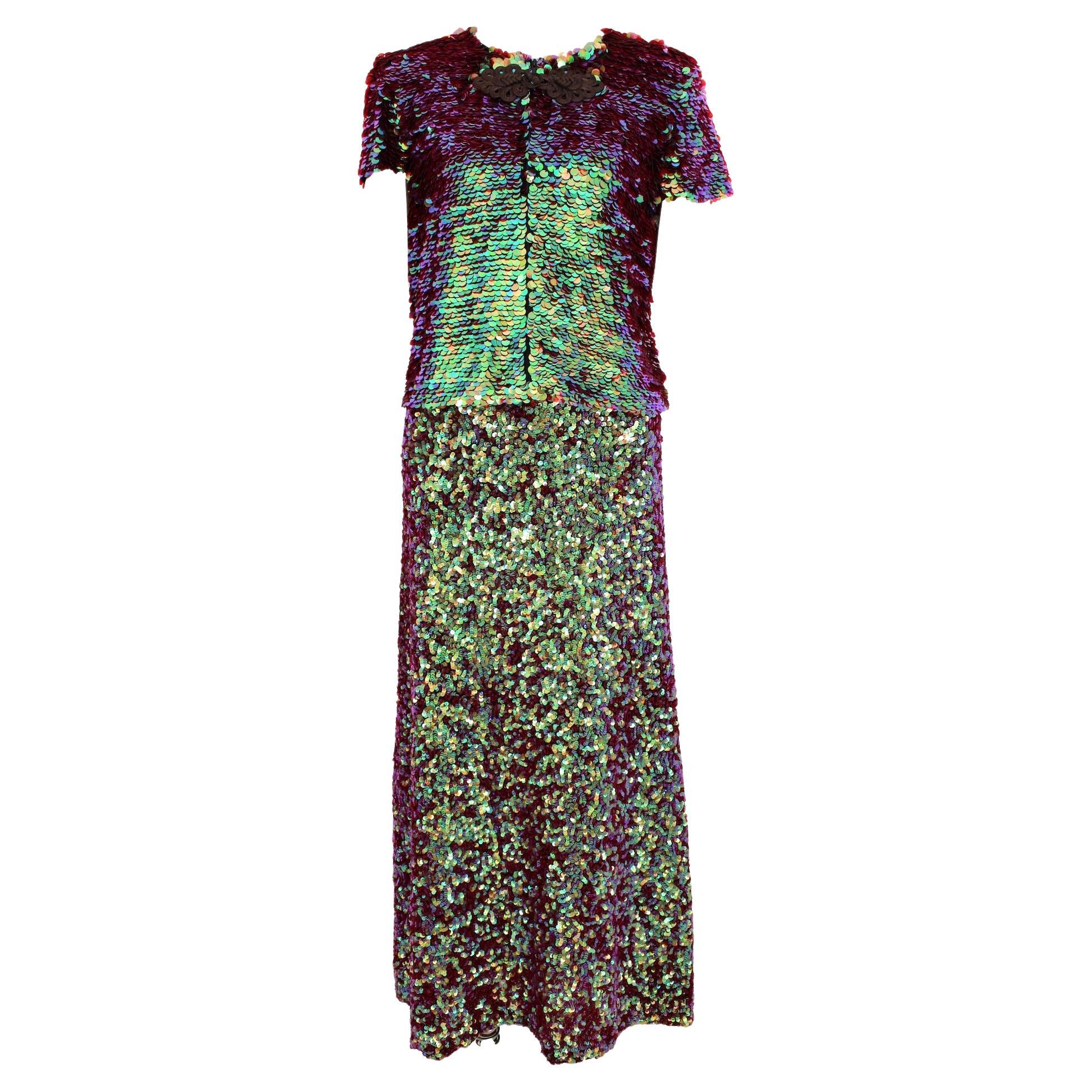 This is a vintage 90s Jean Paul Gaultier skirt suit that is perfect for evening wear. The suit features a long skirt with iridescent sequins in a variety of colors that create a beautiful, eye-catching effect. The short bolero jacket also features