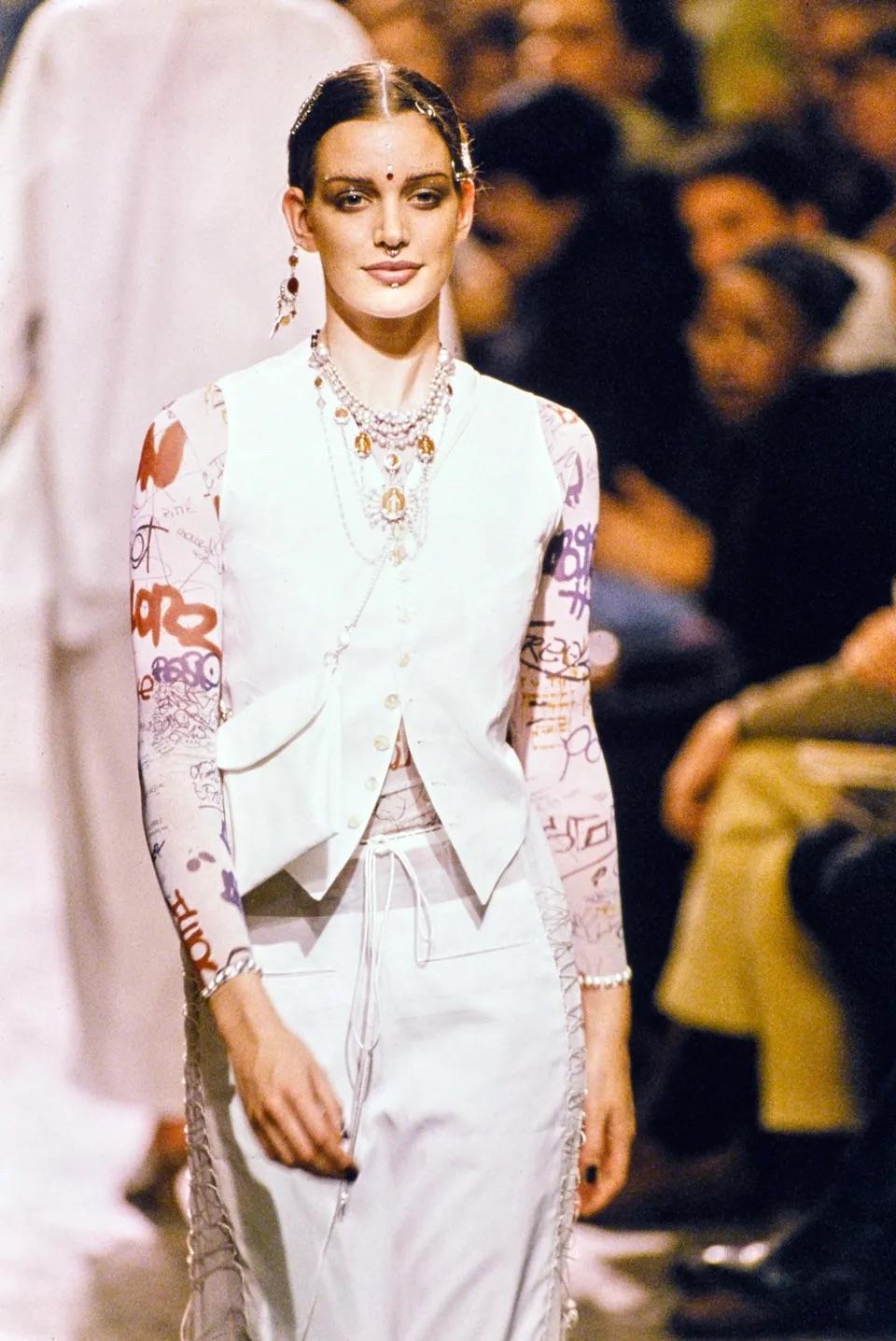 Jean-Paul Gaultier mesh long sleeves top and matching mesh long wrap skirt from Spring Summer 1994 “Les Tatouages” collection as seen on the runway. Both pieces have a graffiti colourful print all over. Top is embellished with studs on the neckline
