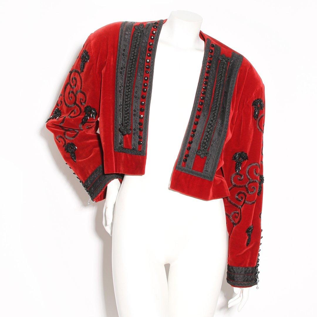 Product Details:
Velvet bolero by Jean Paul Gaultier 
Winter 1985 RTW collection
Red velvet 
Black rope trim 
Black floral ribbon 
Embroidered swirls embellishments 
Black beading 
Silver and black-tone hardware 
Zipper cuff closure
Crop style 
Open
