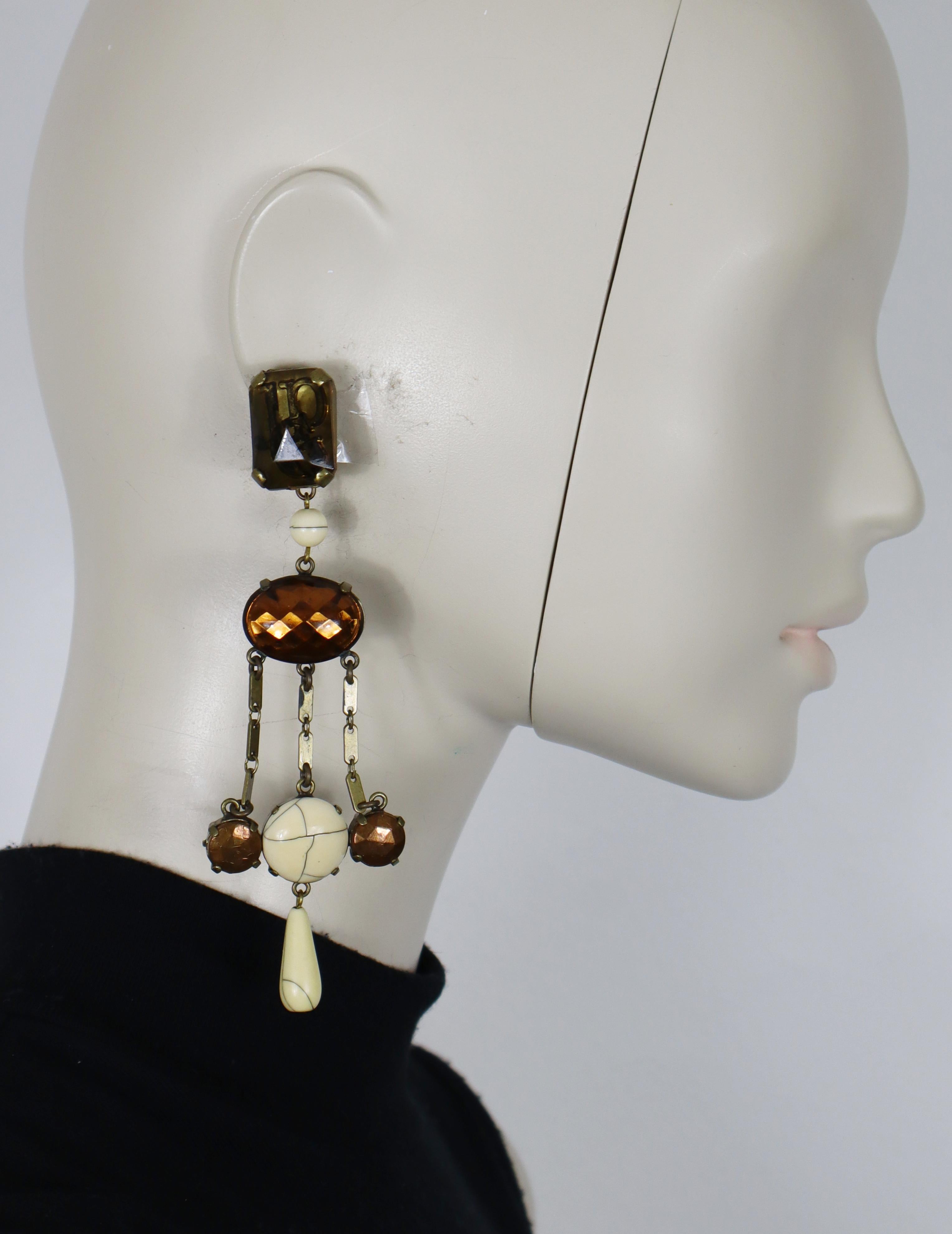 JEAN PAUL GAULTIER Vintage-Ohrringe mit langem Kronleuchter (Clip-on) mit eingelegtem JPG-Logo aus Harz, kupferfarbenen Harzcabochons, cremefarbenen Harzcabochons, Perle und Tropfen.

Metallbeschläge in antikem Bronzeton.

Auf den Rückseiten mit JPG