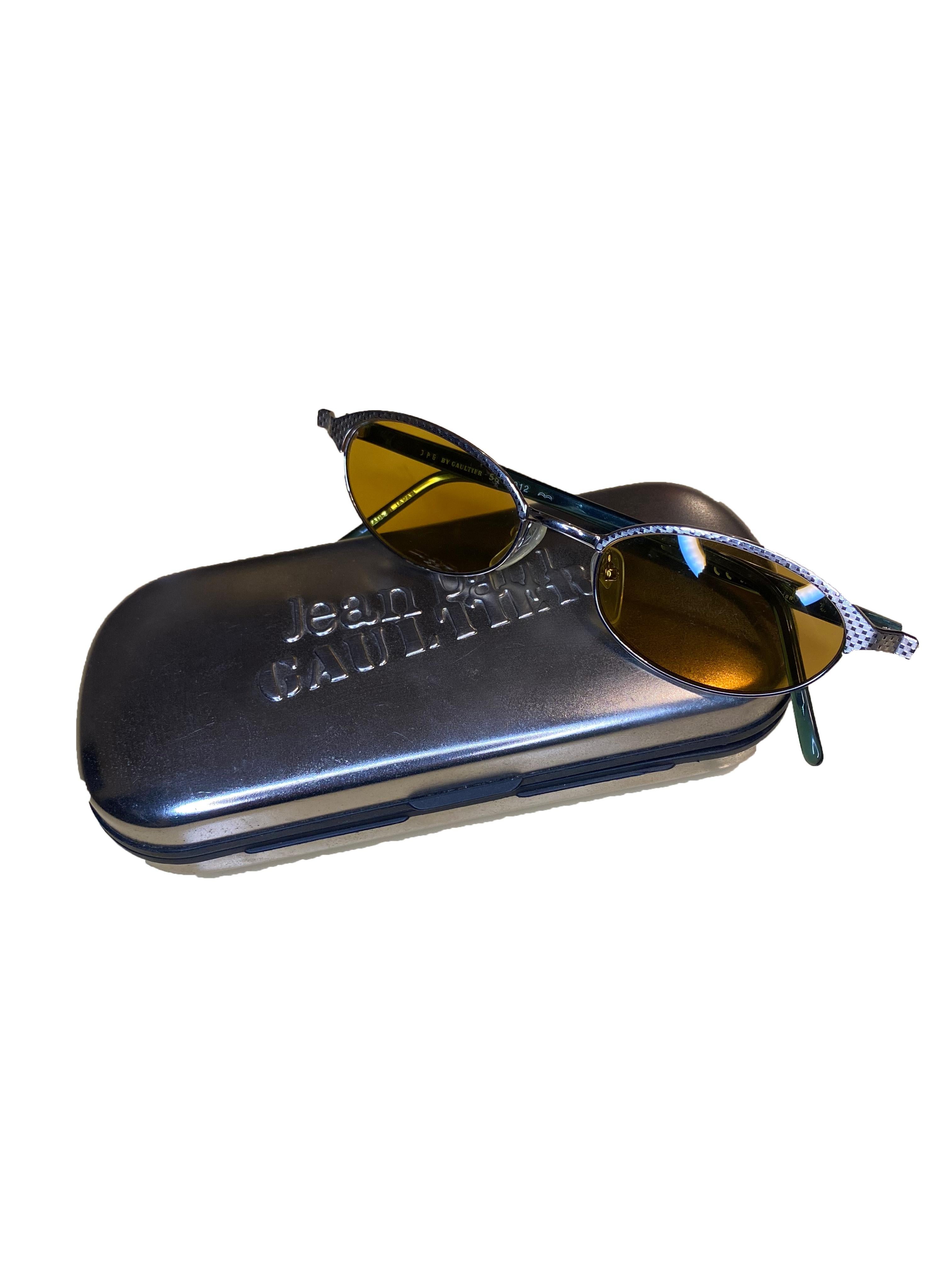 Lunettes de soleil vintage de Jean Paul Gaultier. Cadre oblong en métal argenté avec un léger motif texturé. Teinte jaune sur les lentilles. Pieds étroits en acétate vert/bleu avec le même motif. Logo JPG embossé sur l'extérieur des jambes. Marquage