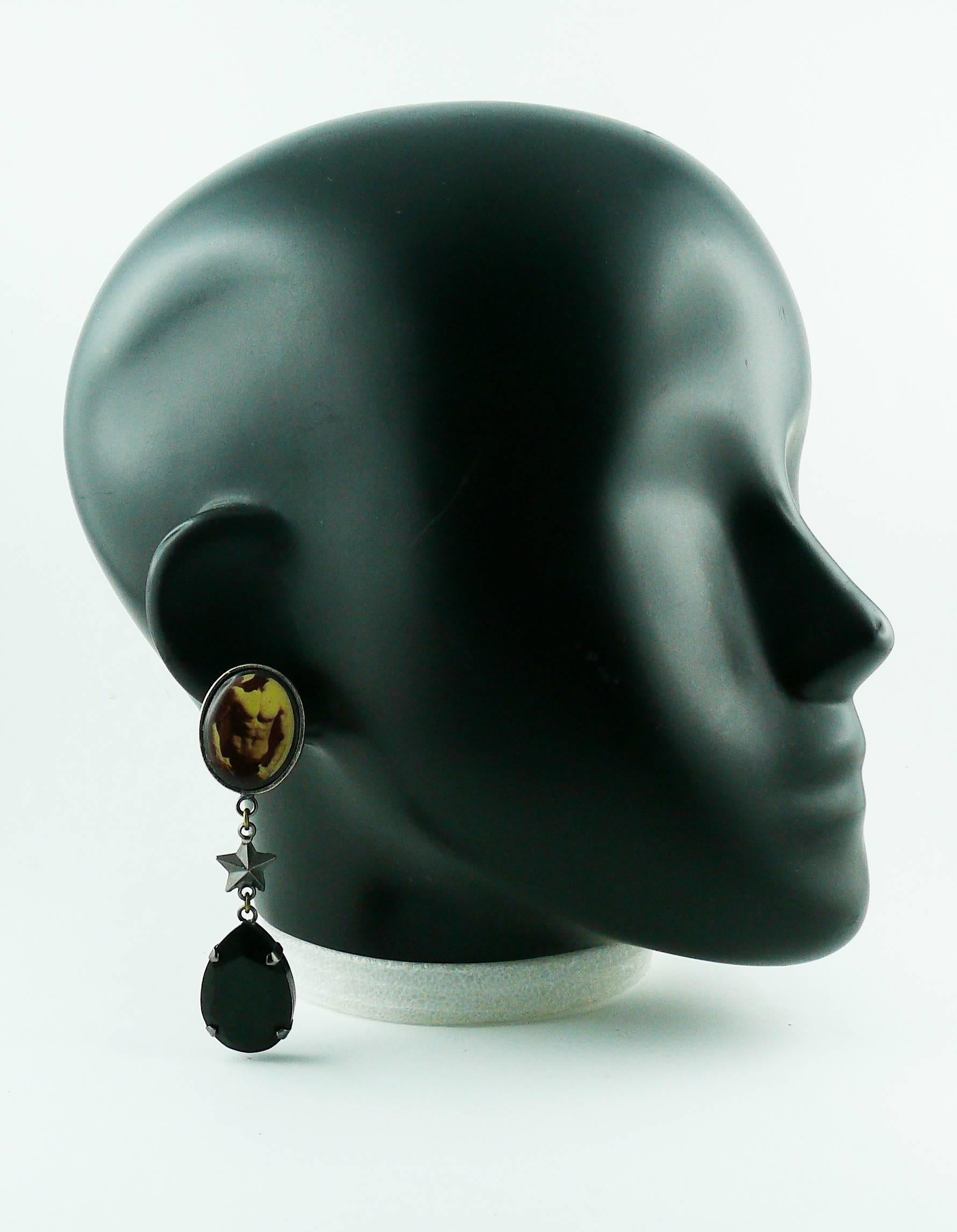 JEAN PAUL GAULTIER vintage novelty dangling earrings (clip-on) featuring a resin inlaid male torso print top and a large black crystal drop in a gun patina metal setting.

Marked JPG.

Indicative measurements : length approx. 8.4 cm (3.31 inches) /