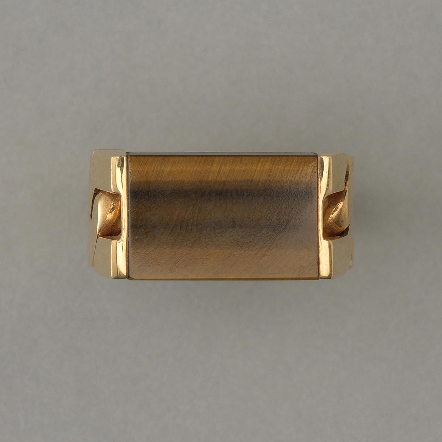 A sleek 18 carat yellow gold ring set with a rectangular tiger eye slab that is held by one curb link made by the French master goldsmith Jean Pierre Brun, 1970.  

Brun used to work for Cartier, VCA and Chaumet and in the 1990s Brun also worked on