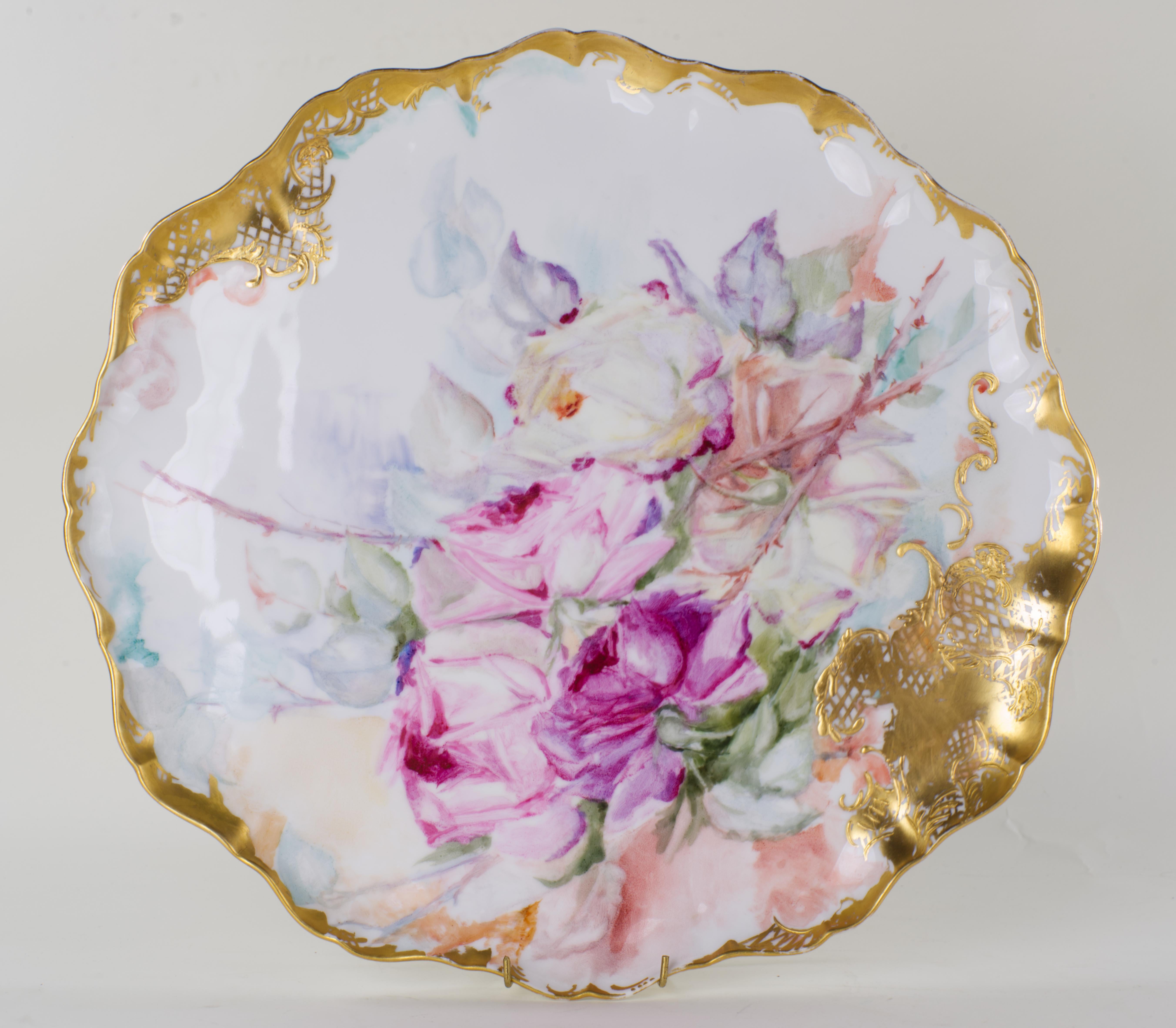 Le grand plateau ovale en porcelaine est peint à la main d'un bouquet de roses dans différentes nuances de rose et décoré d'une bordure dorée asymétrique. Le plateau a un fond en biscuit non émaillé ; un bord bas et ondulé s'étend autour du plateau,