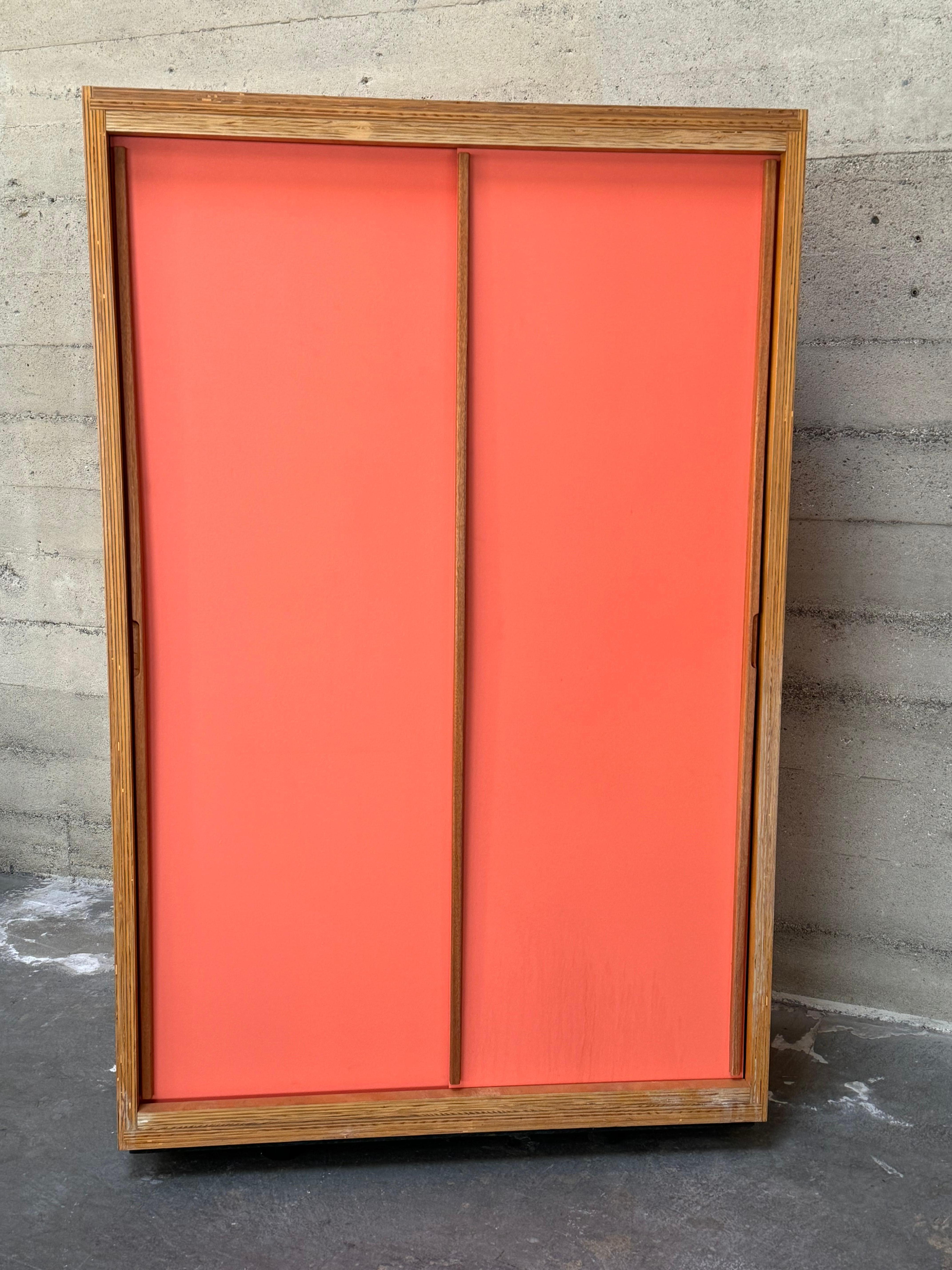 Jean Prouve style cabinets constructed of high grade figurative plywood. With a statuesque present and scale, a true and unique stand out. The two sliding doors are in a salmon pink color with pulls that extend from top to bottom of the cabinet and