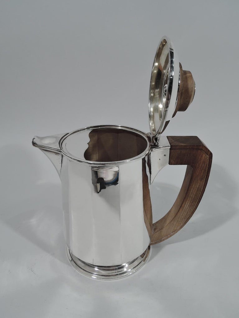 French Art Deco 950 silver coffeepot, circa 1930. Faceted cylinder on round and stepped foot. Covered “fish mouth” v-spout. Wood scroll-bracket handle. Cover hinged and raised with round and stepped finial; finial top has silver circle engraved with