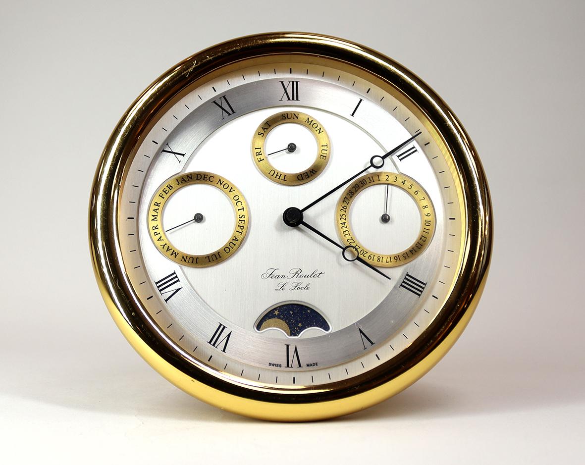 A beautifully gilded desk clock with perpetual calendar and moon-phase, made by Jean Roulet, Le Locle in Switzerland.

The early quartz movement is housed behind the brushed silver dial which displays the date, month and day of the week with the