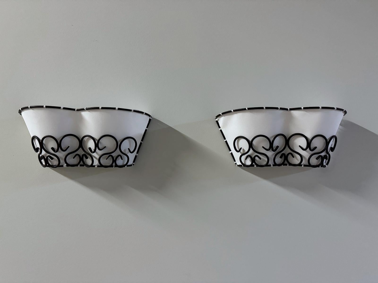 Two beautiful French designer wall lights hand made in 1960s in the style of world design genius, Jean Royère. Featuring a wrought iron frame with a off white canvas  shade.
Fully working and tested condition with two E14 Edison socket, the lamp