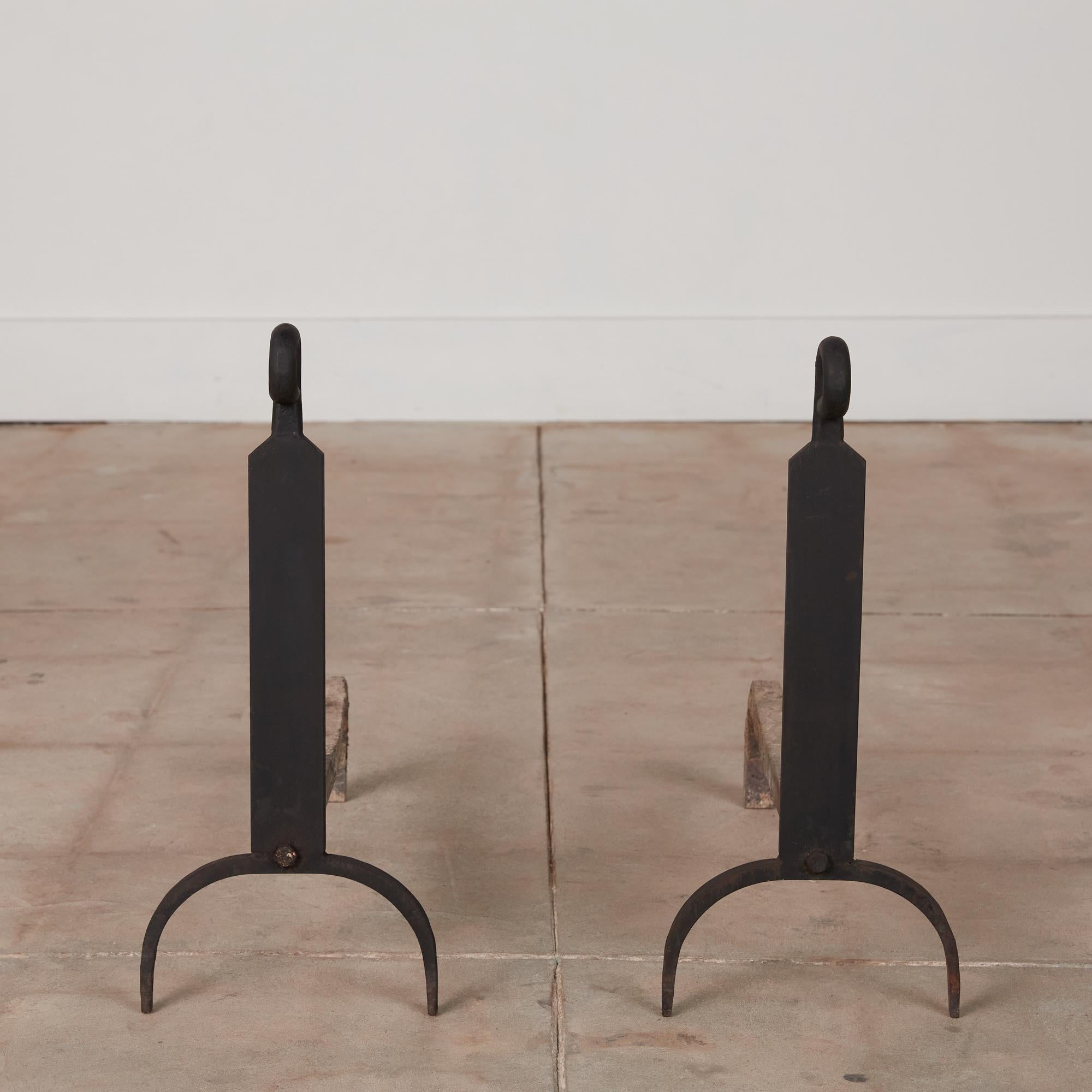 An excellent pair of cast iron Jean Royère style andirons. The andirons feature a patinated 