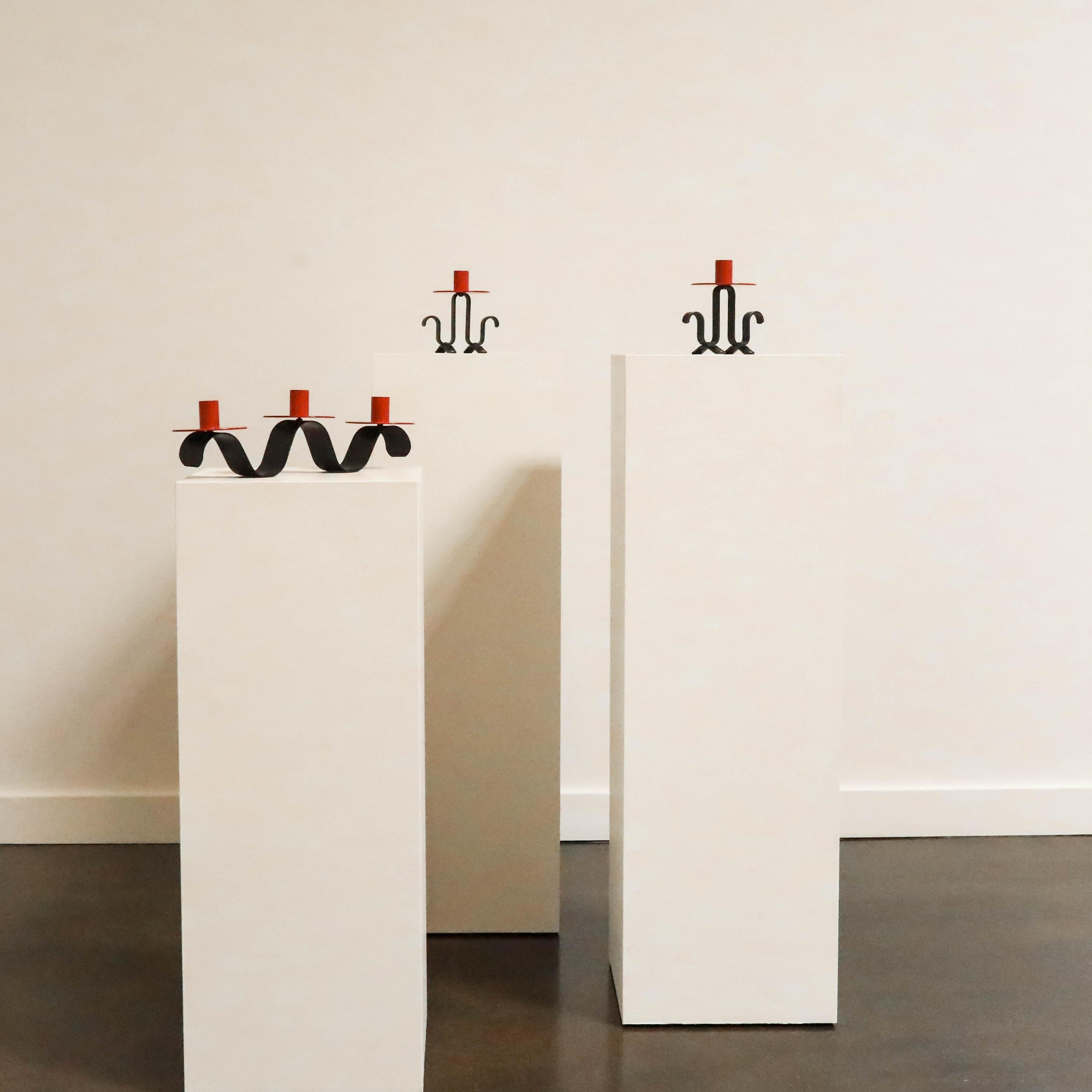 Un set di portacandele in metallo laccato rosso e nero nello stile di Jean Royère. Le forme scultoree e inanellate evocano un senso di movimento giocoso, caratteristico della miscela di estro e modernismo che contraddistingue Royère. Un accento