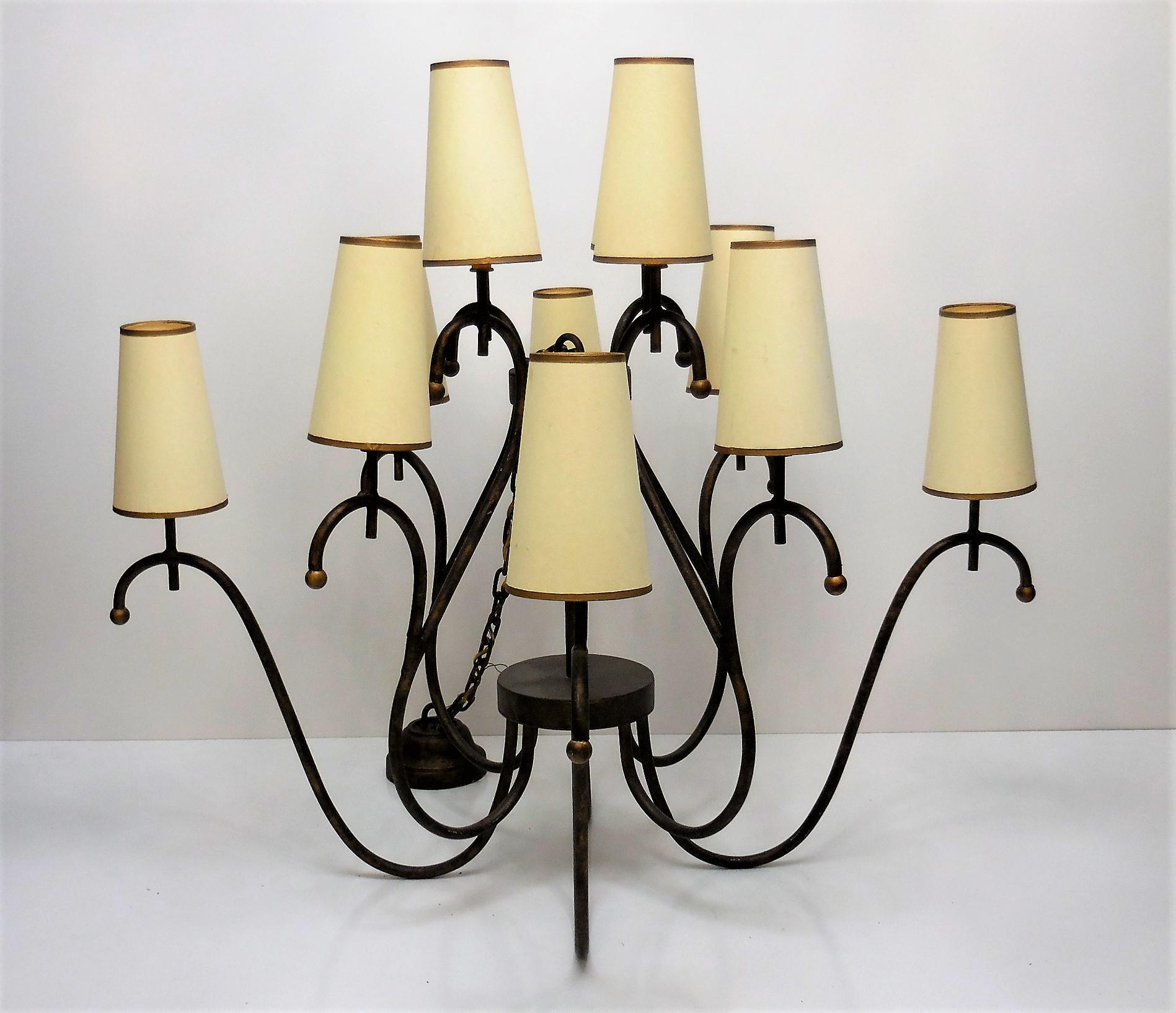 A very large chandelier. Metal frame with a cold bronze patina. 12 conical paper shades with gold trim sit on the crest of the arms. Retains chain, custom mounting hardware and ceiling plate. The chandelier is 42