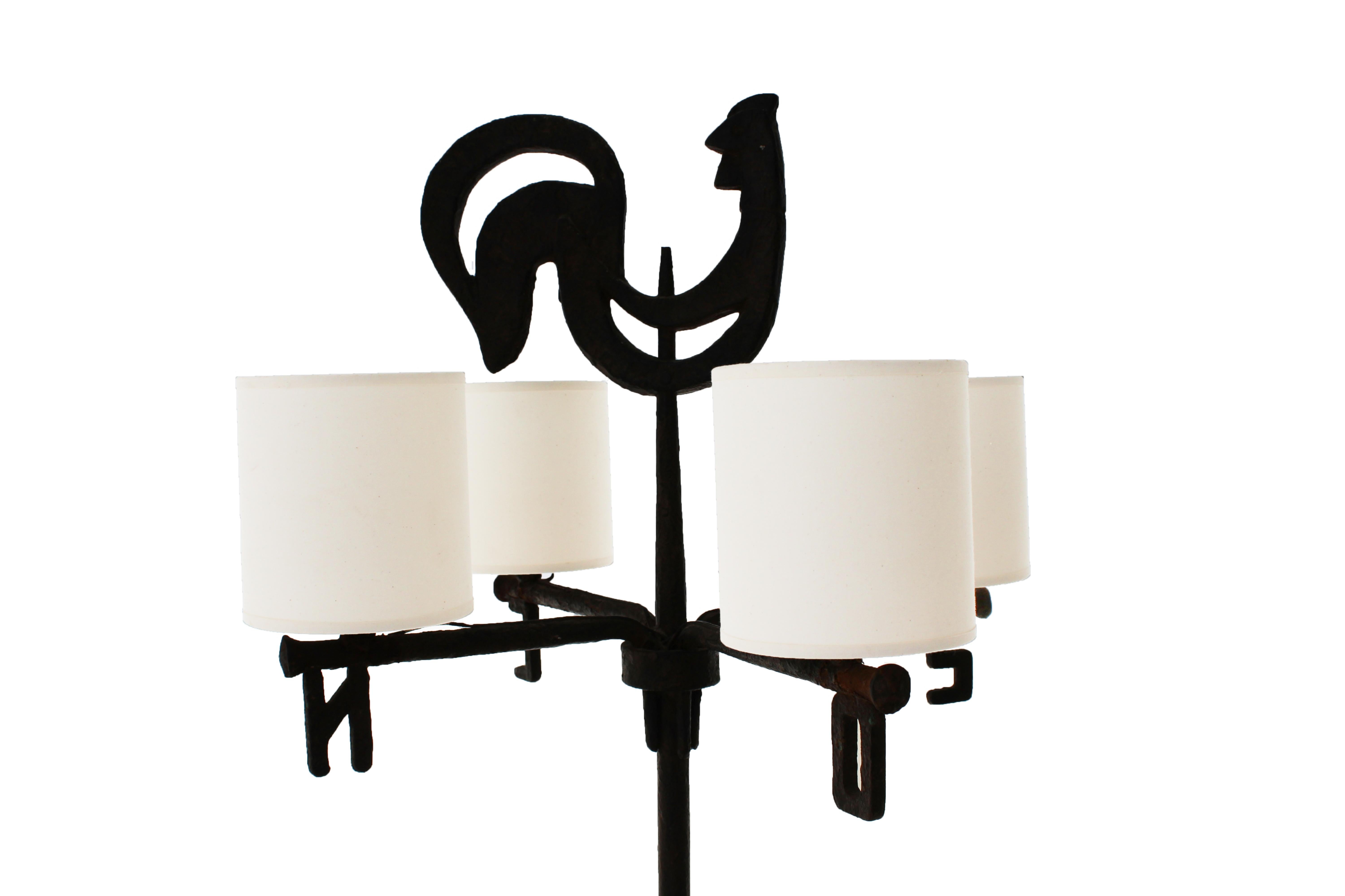 Jean Touret (1916-2004) for the Marolles workshop,
Four-light floor lamp model « Girouette »,
Wrought iron beaten with rooster decoration and under each light the initial of the four cardinal points,
Tripod base,
With four lampshades, 
Circa