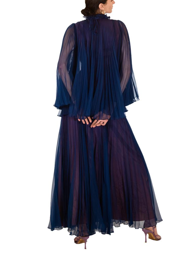 Striking Jean Varon 1970s evening dress. Navy blue pleated chiffon gathered into the ruff collar at the neck forming a cape effect is then echoed in the skirt. The purple lining gives depth and drama.

Original 1970's. Jean Varon label. Excellent