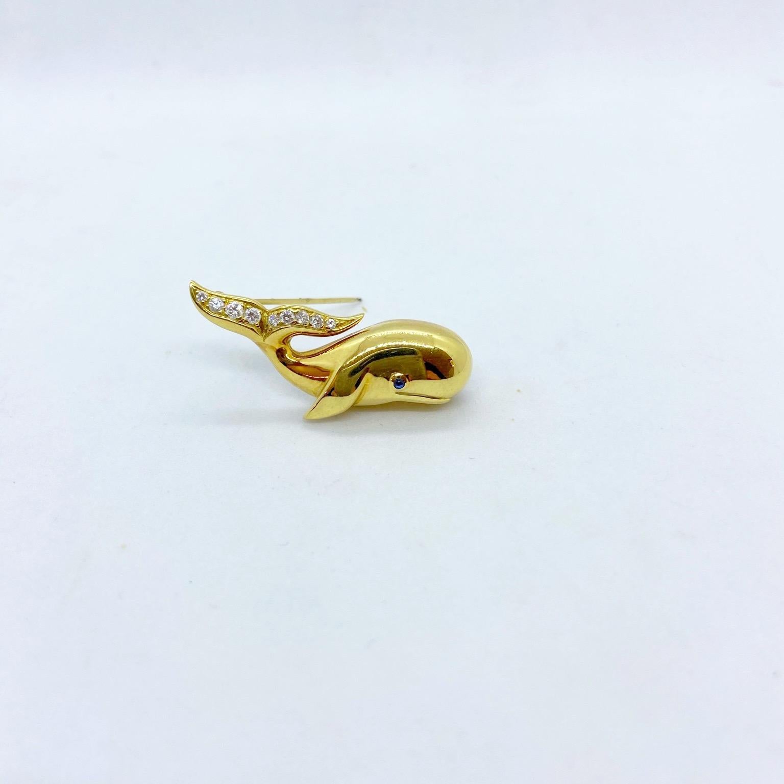 An adorable whale brooch crafted in a hi-polished 18 karat yellow gold. The smiling whale has a blue sapphire eye and a tail set with 0.23 carats of round brilliant diamonds. The whale measures 1.5